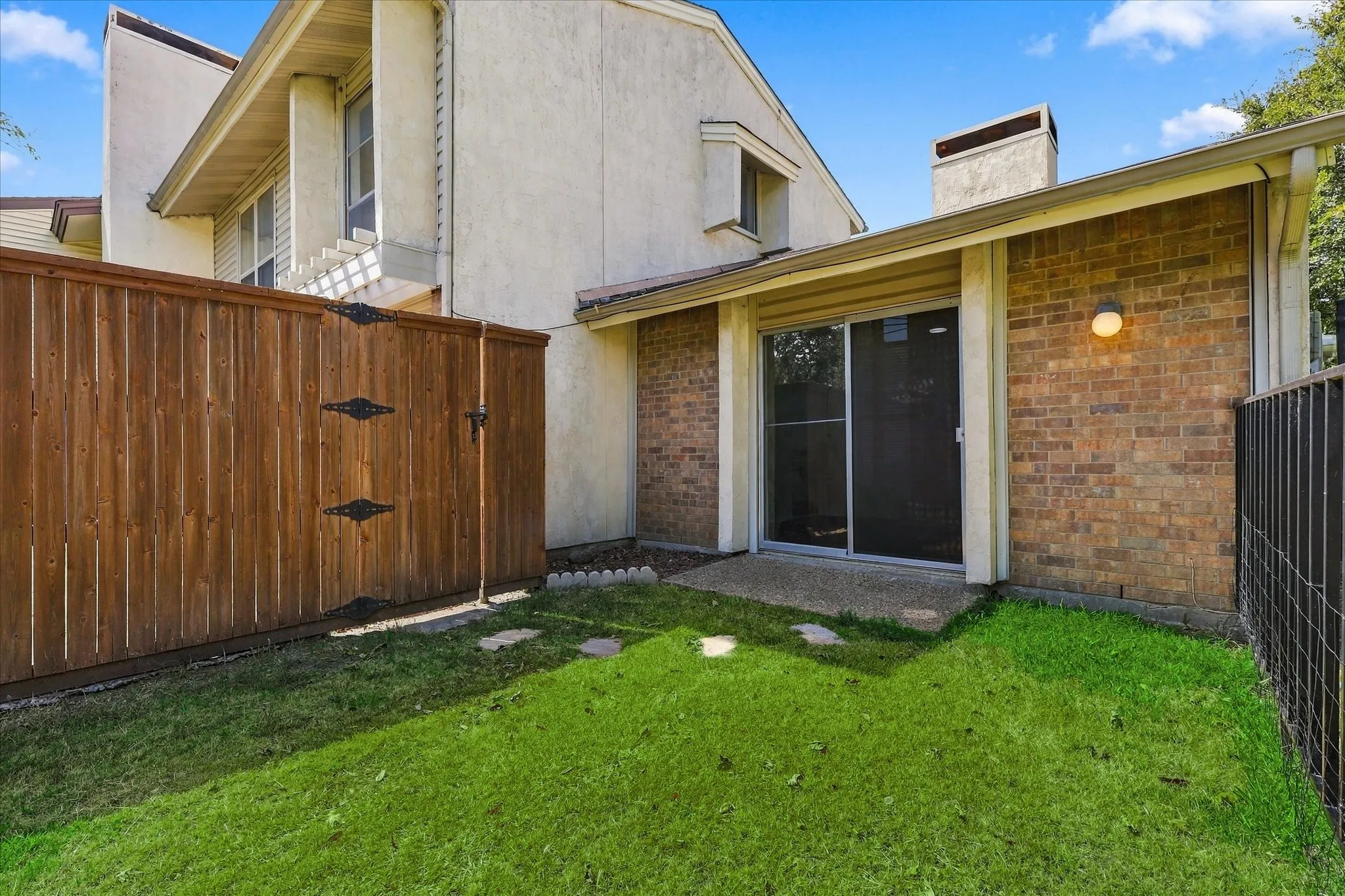 Private backyard featuring a wood privacy fence with gate, brick exterior, sliding glass door, and a grass area