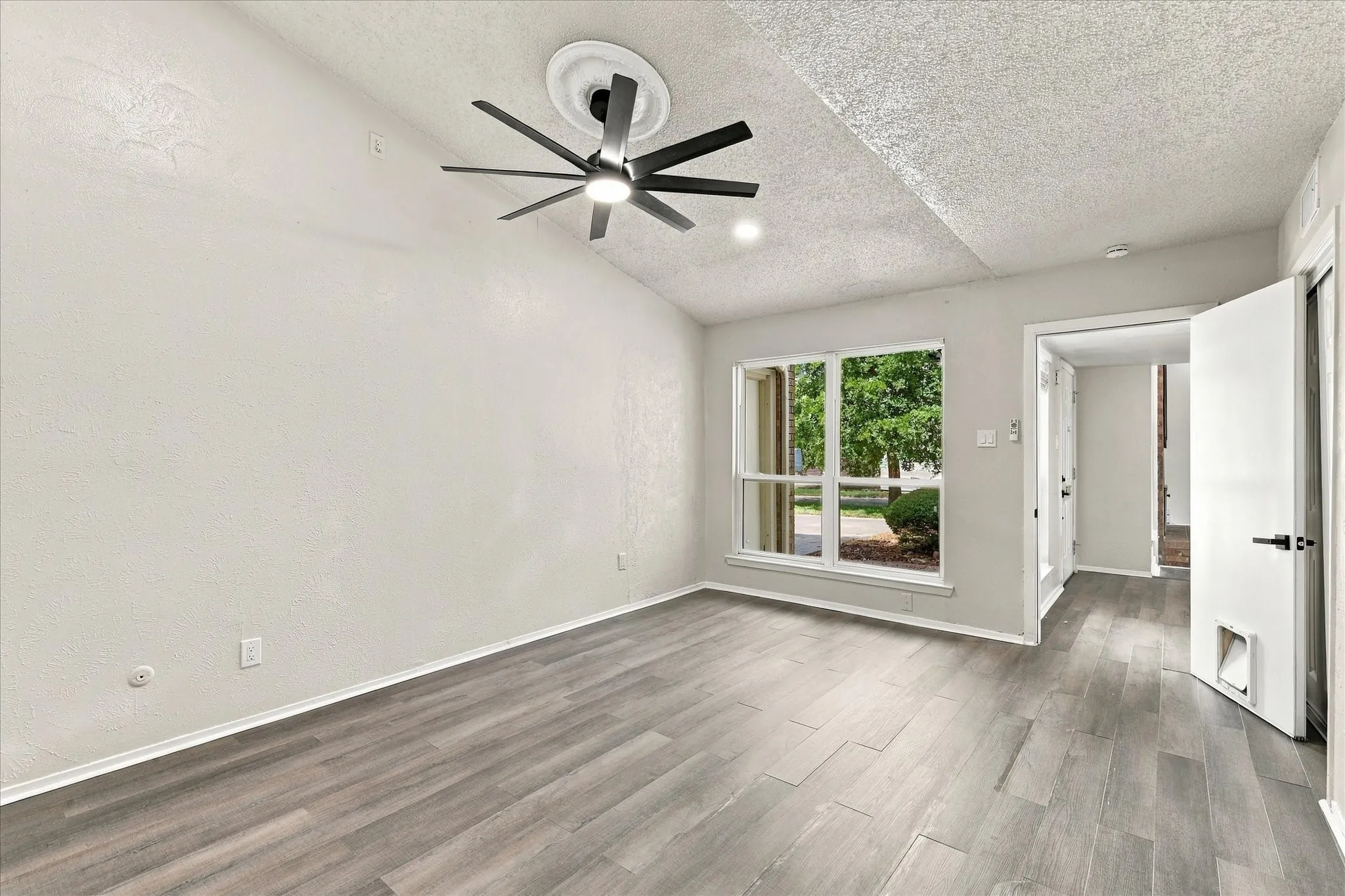 Vaulted ceiling with a modern ceiling fan, wood-finish flooring, and a large window