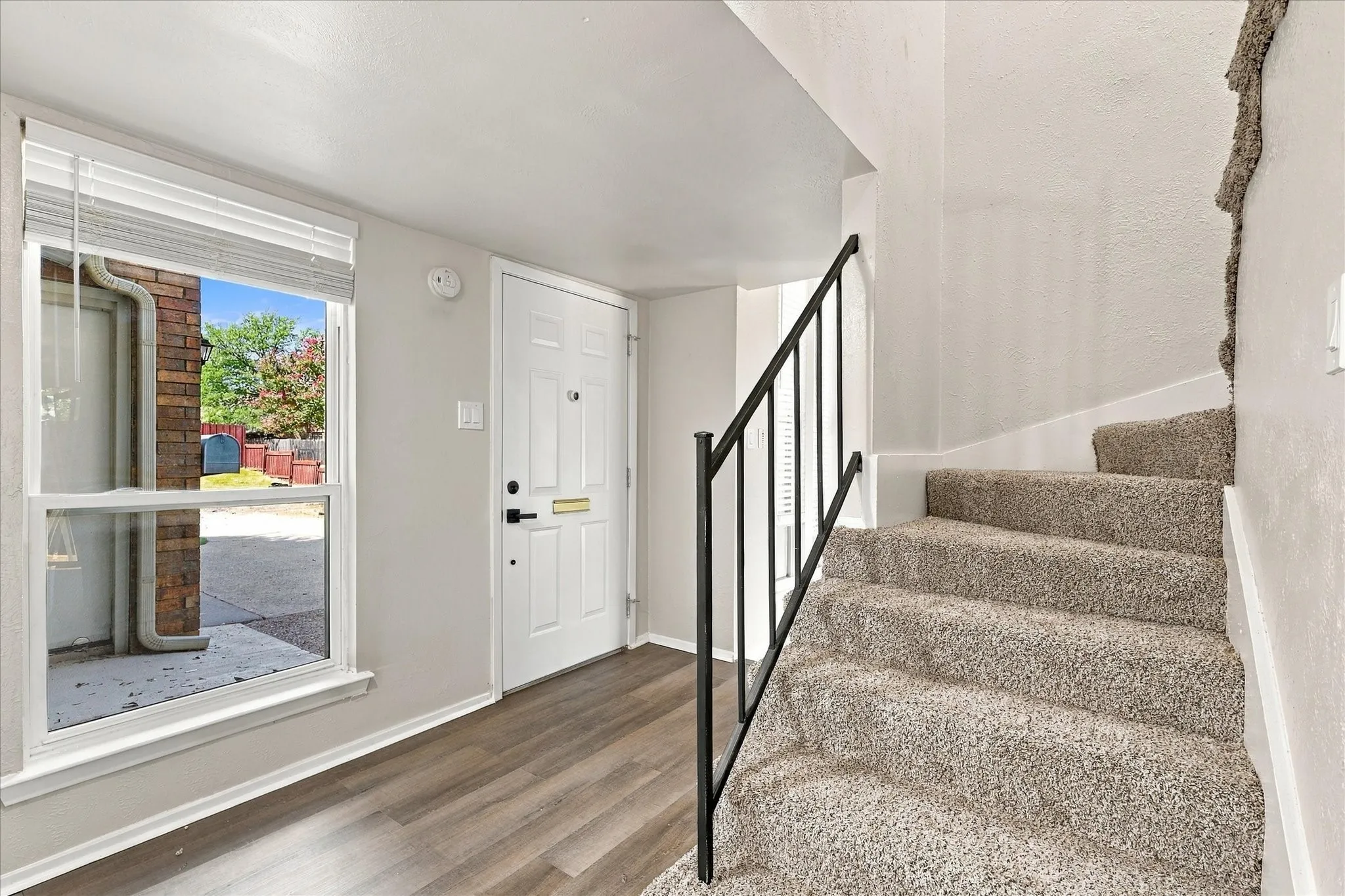 Entryway featuring wood-finish flooring, white paneled door, and a staircase with carpeted treads and a black metal handrail