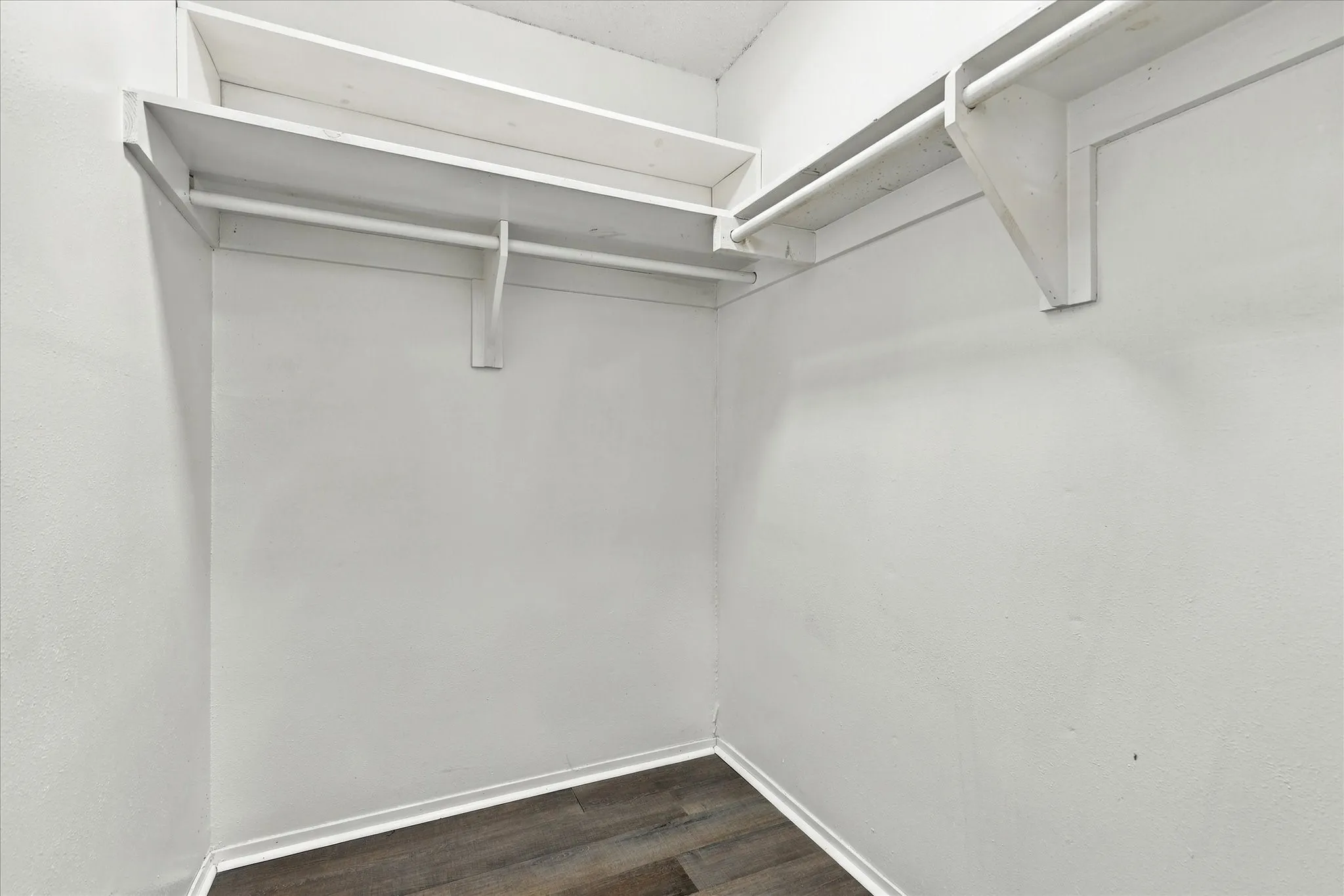 White interior walls, multi-tier shelving, clothing rods, wood-finish flooring, and white trim