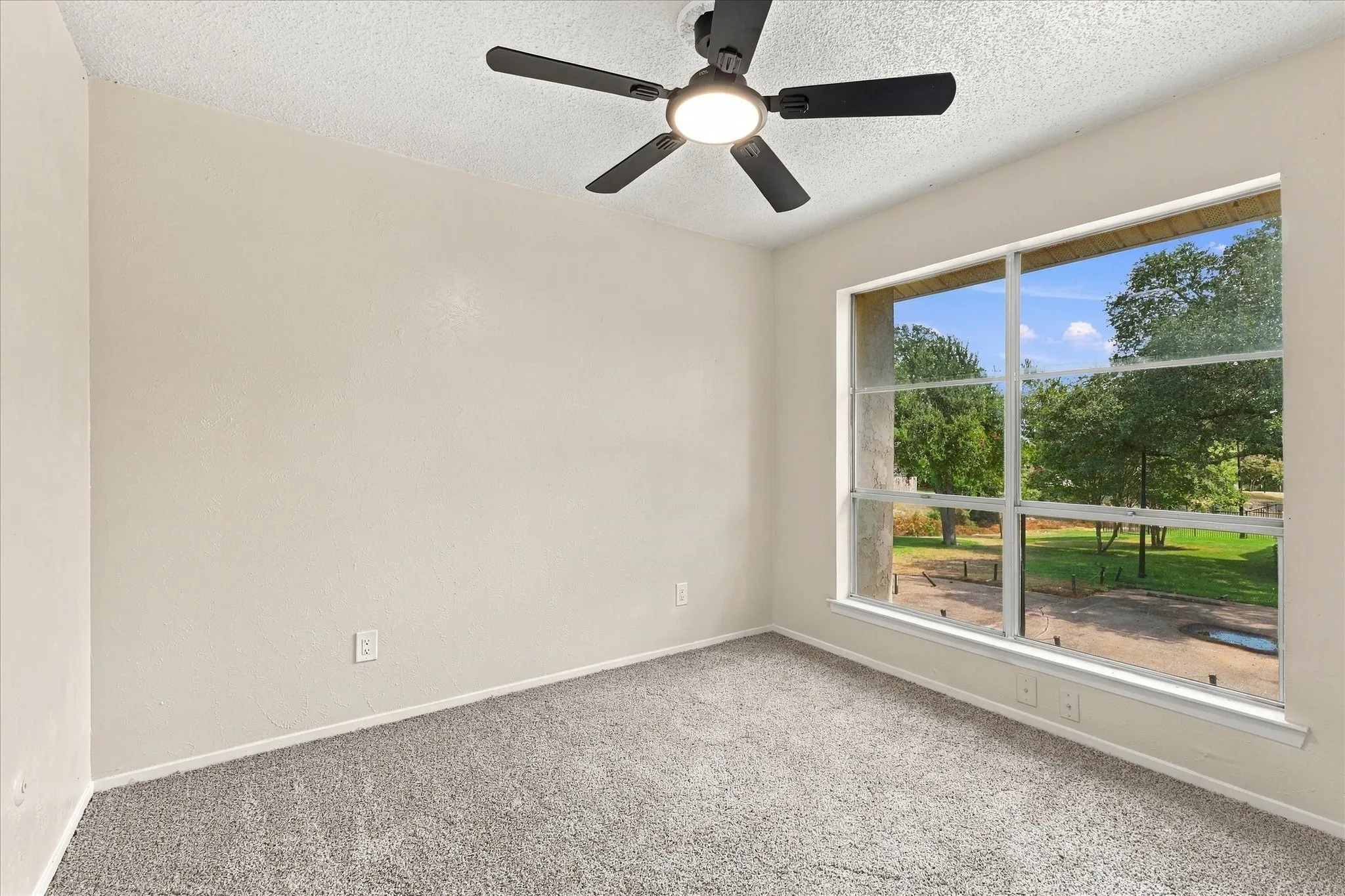 Wall-to-wall carpeting, large window with outdoor scenery, and a ceiling fan with integrated lighting