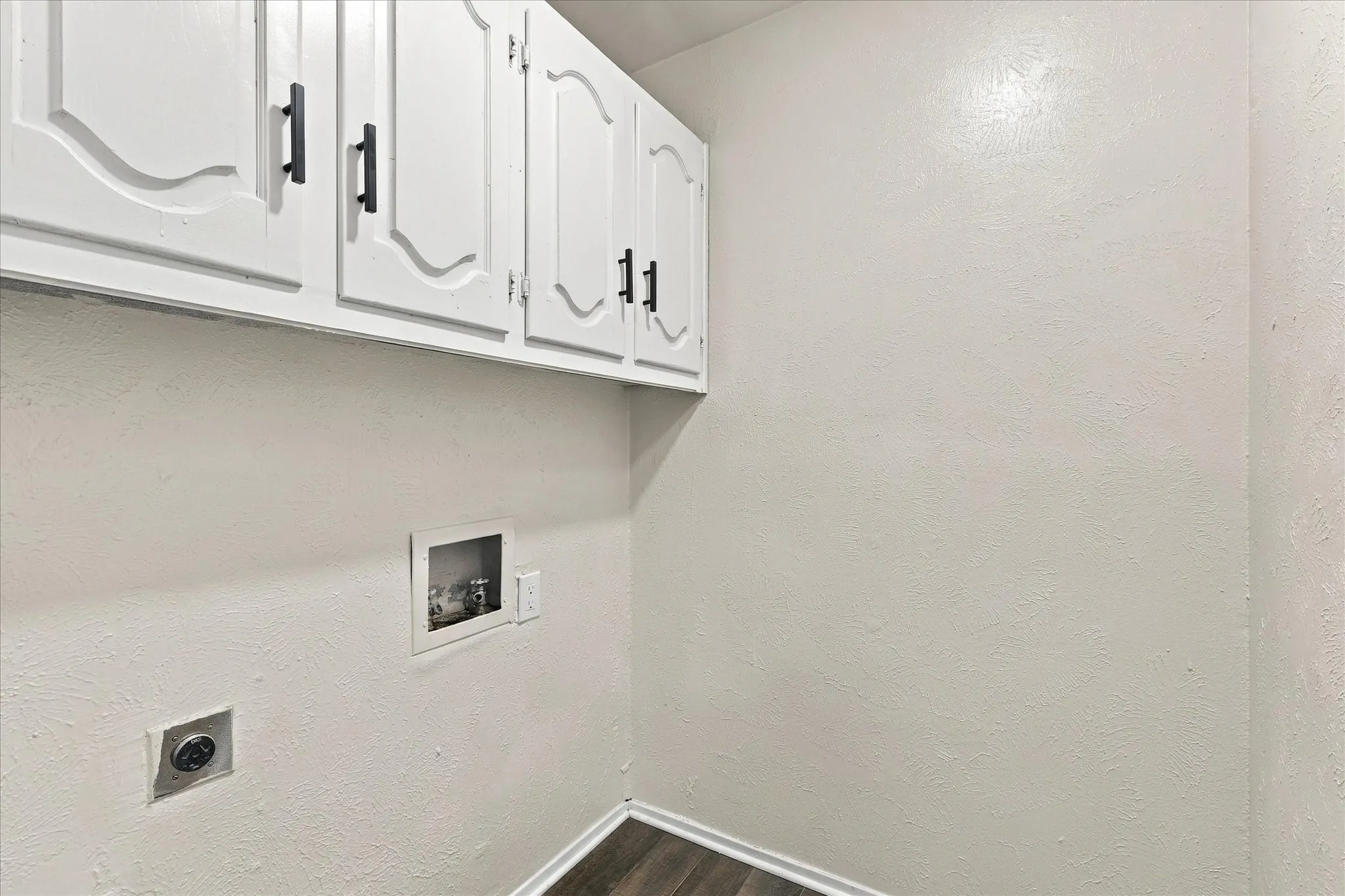 White upper cabinetry with black hardware, wood-finish flooring, and laundry hookups