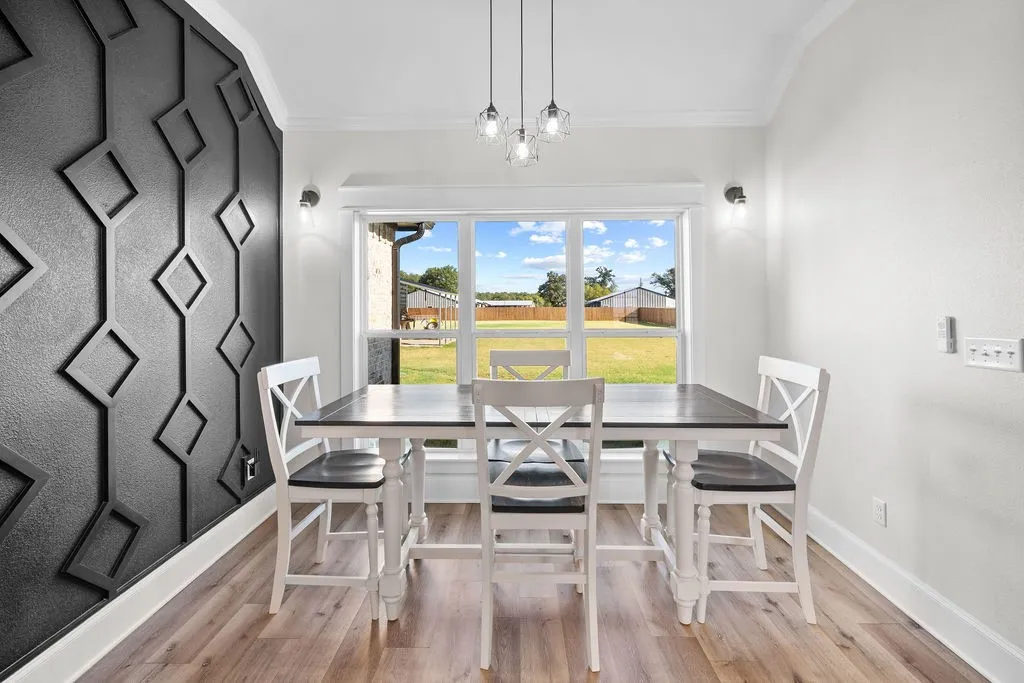 Accent wall with geometric trim, wood-finish flooring, large picture window, crown molding, and contemporary pendant lighting