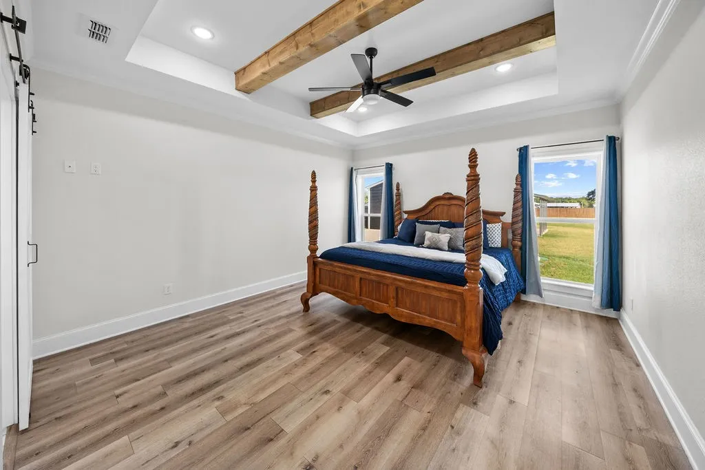 Tray ceiling with recessed lighting and wood beams, wood-finish flooring, two windows, and a barn door