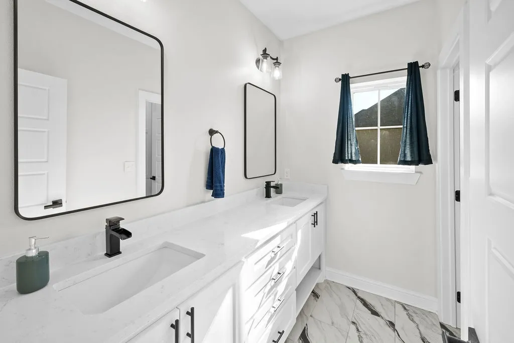 Dual vanity with integrated sinks, white cabinetry, matte black hardware, and an expansive countertop