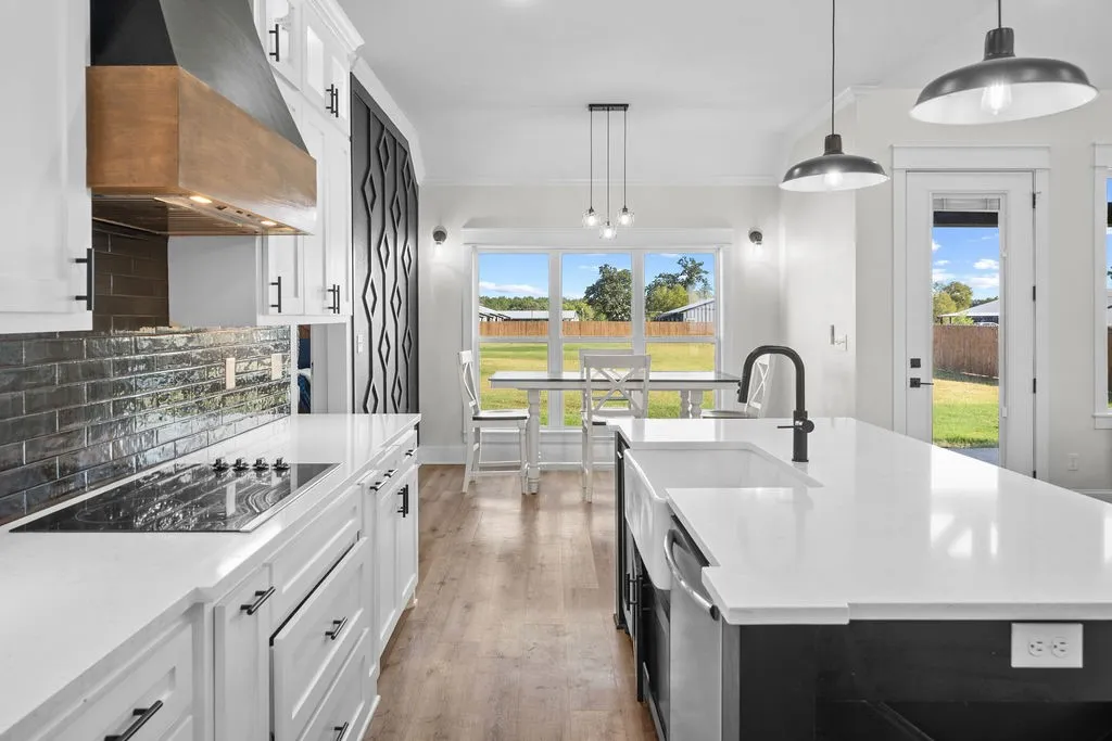 White shaker cabinetry, integrated cooktop, white solid surface countertops, farmhouse sink with matte black faucet, and wood-finish flooring
