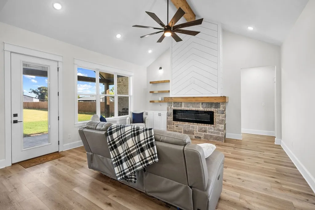 Vaulted ceiling with exposed wood beam, stone fireplace with a wood mantel, wood-finish flooring, recessed lighting, and large windows