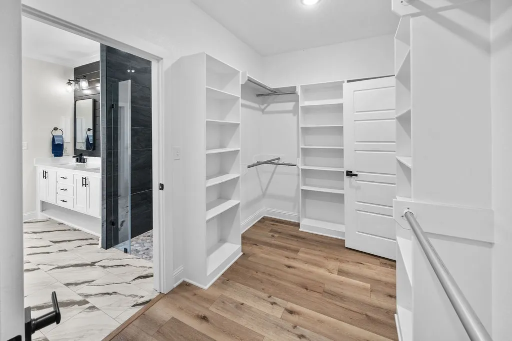 Custom built-in shelving, wood-finish flooring, white paneled door, and brushed nickel hanging rods