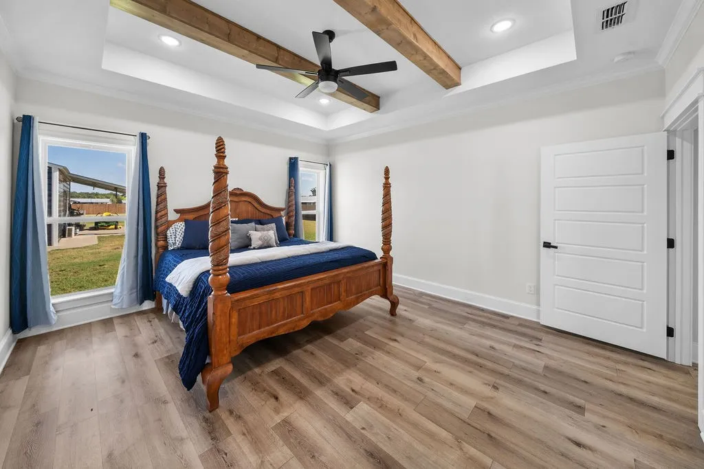 Wood-finish flooring throughout, tray ceiling with recessed lighting, exposed ceiling beams, ceiling fan, and white paneled door with black hardware