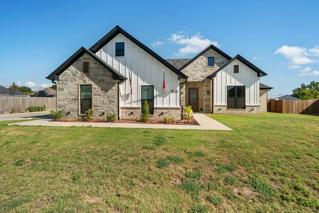 Stone and vertical siding exterior with dark-trimmed windows, a gabled roofline, and a concrete walkway
