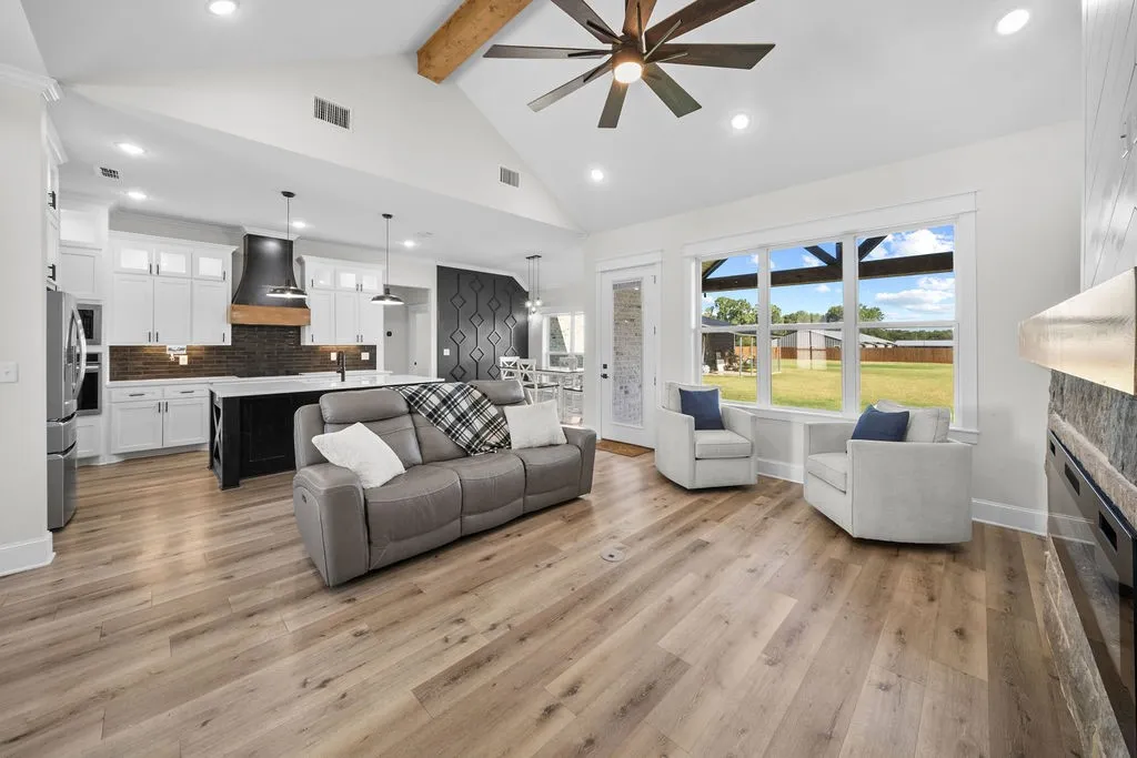 Vaulted ceiling with exposed wood beam, wood-finish flooring, recessed lighting, expansive windows, and a built-in fireplace