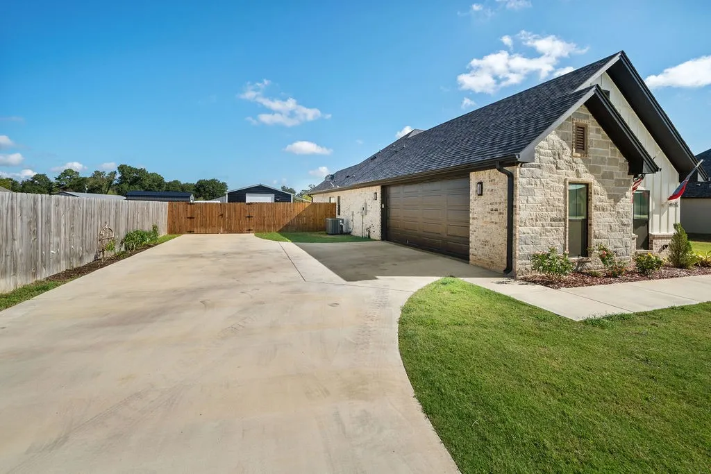 Stone exterior with dark trim accents, attached garage with a dark wood-finish door, concrete driveway, and manicured lawn