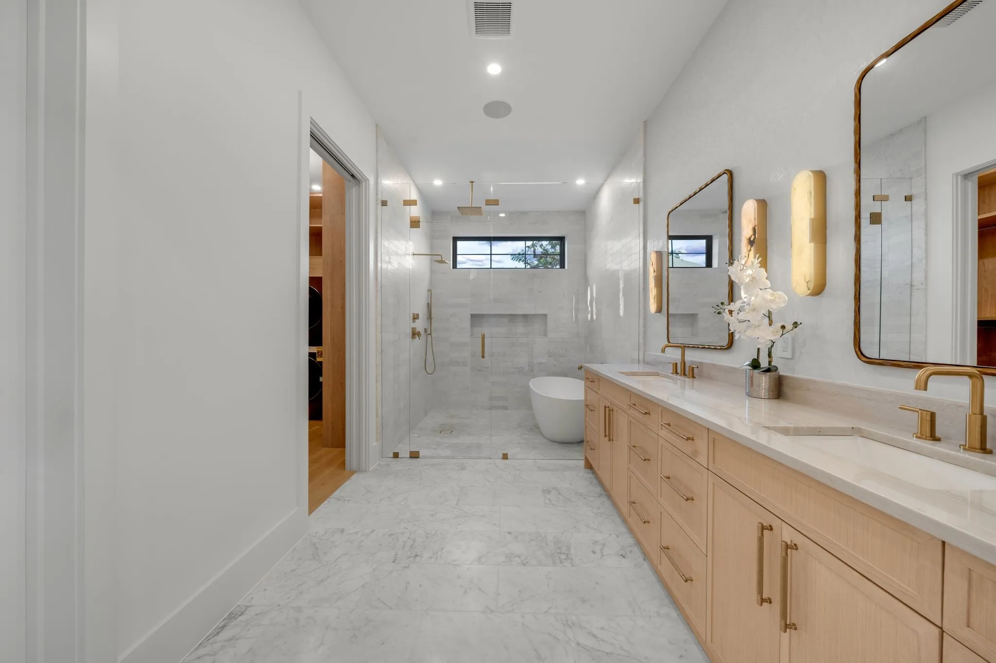 Spacious bathroom featuring a dual vanity with light wood cabinetry, stone countertops, and bronze fixtures