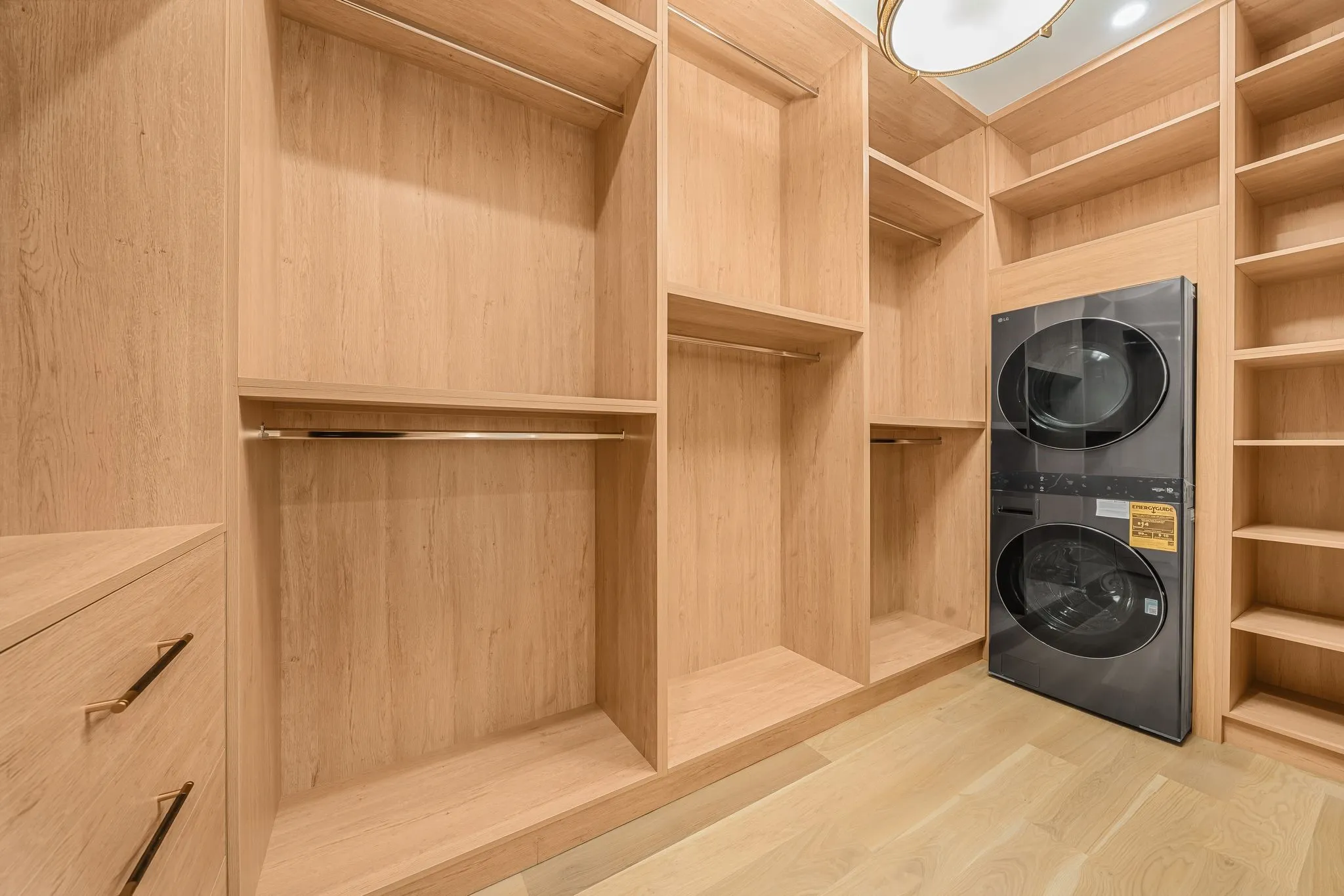 Integrated laundry appliances with custom wood-finish cabinetry, ample shelving, and hanging rods