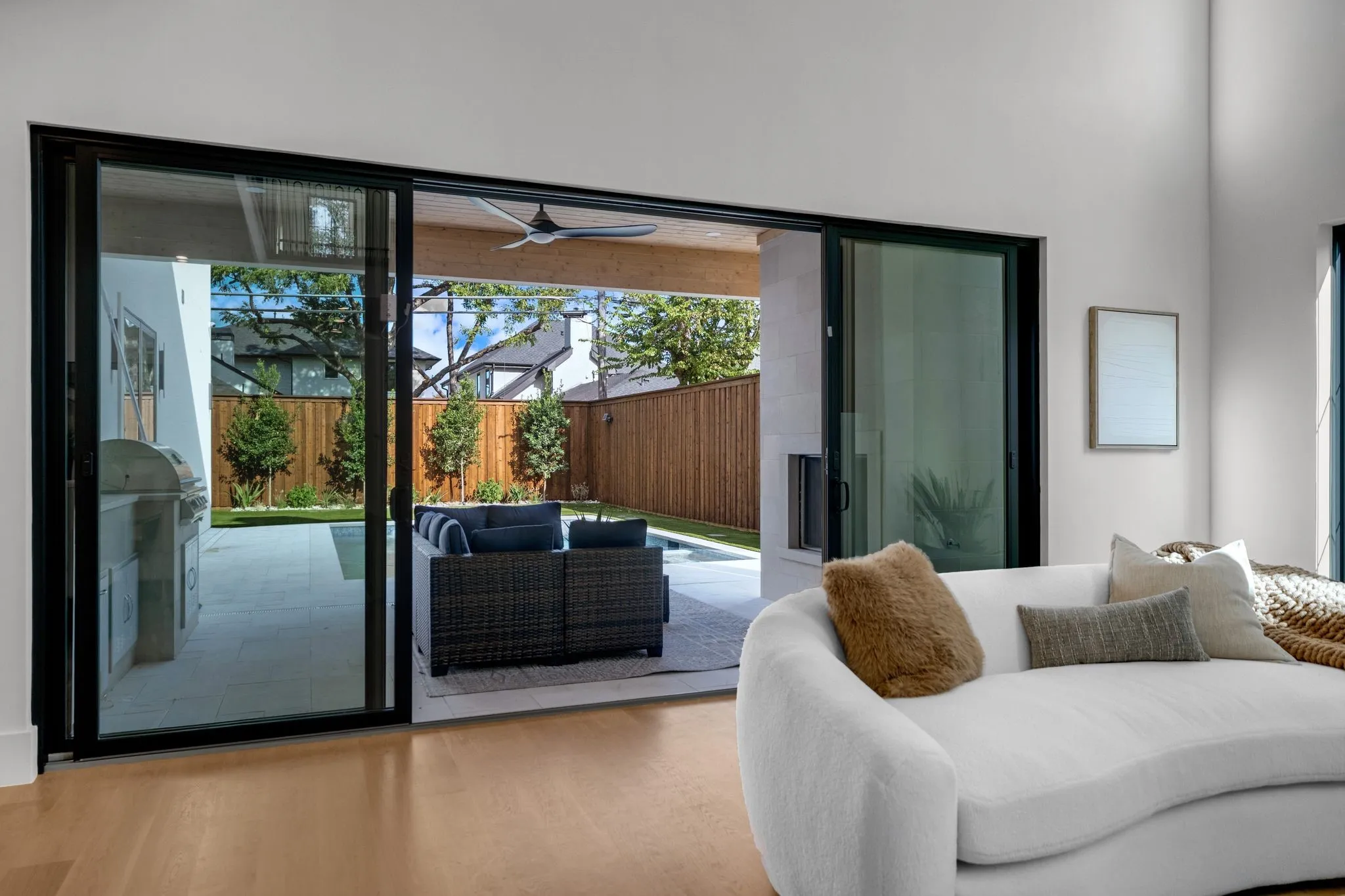 Expansive sliding glass doors open to an outdoor living area with a built-in grill station, ceiling fan, and privacy fencing
