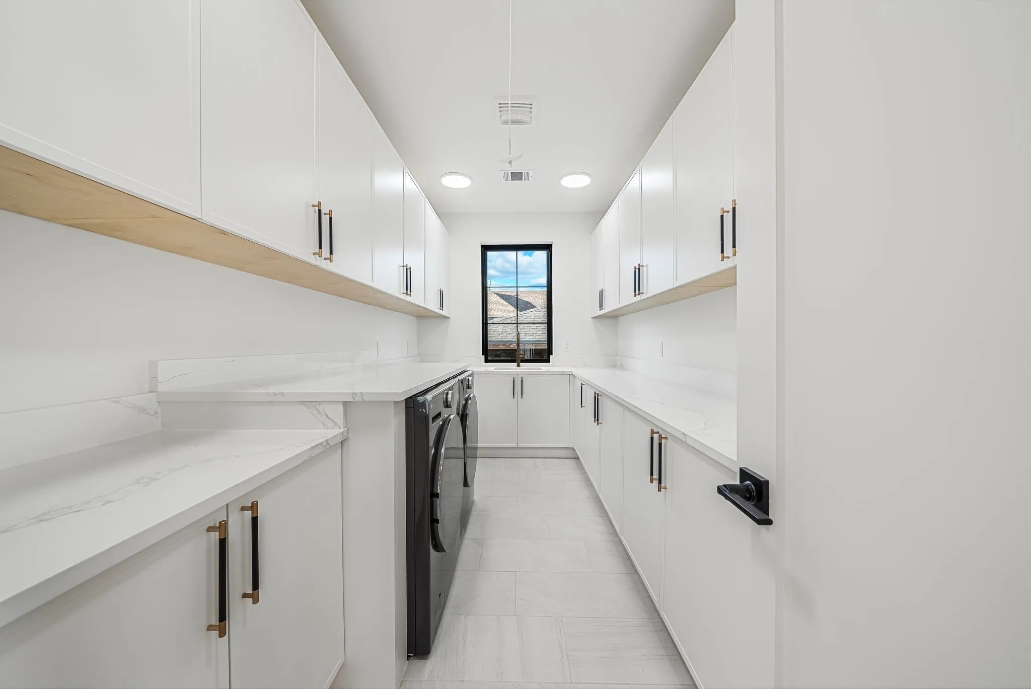 White cabinetry with brass hardware, light wood-finish shelving, and light countertops with integrated backsplash