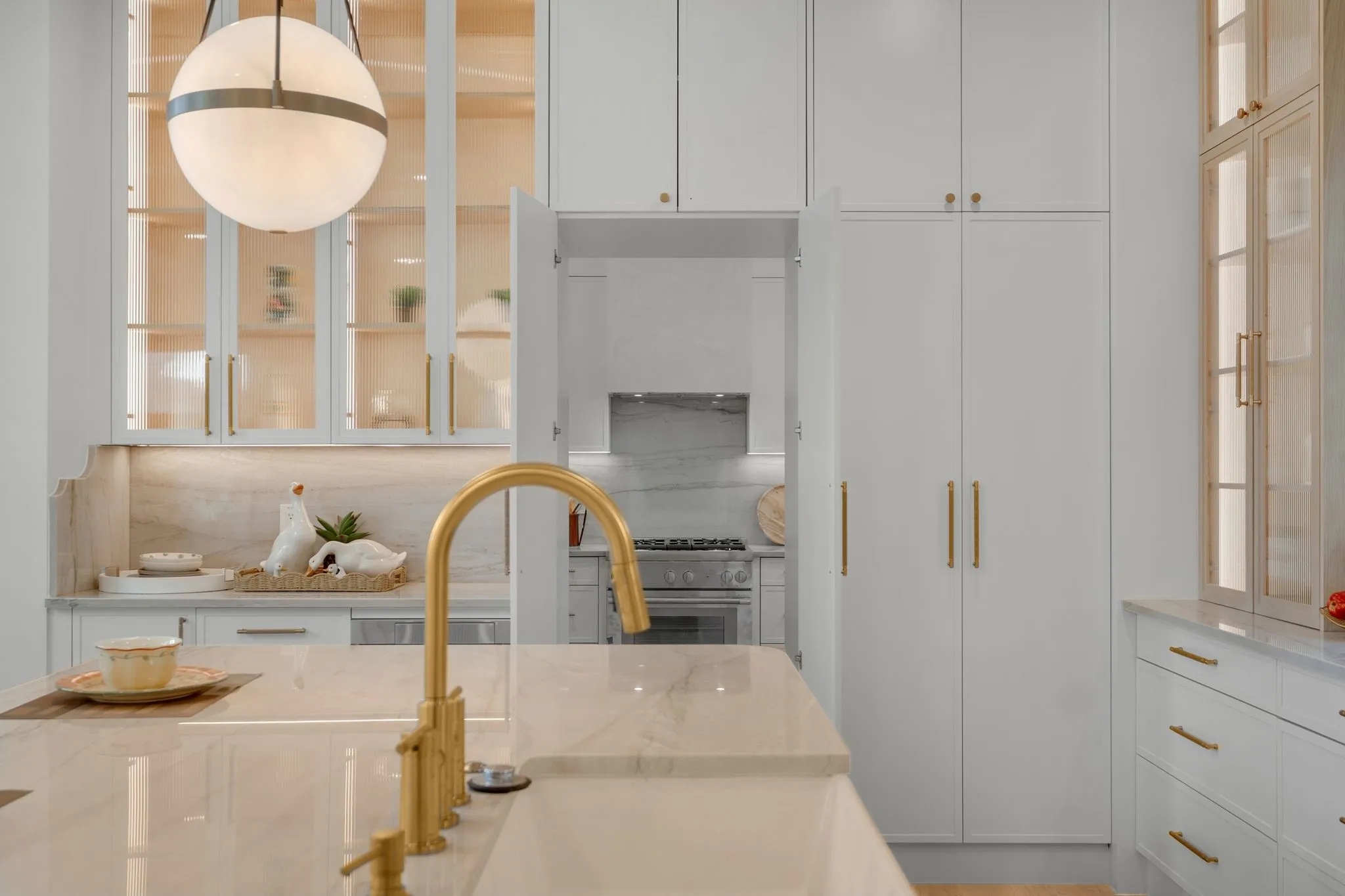 White shaker-style cabinetry with gold-finish hardware, integrated sink with gold-finish faucet, white countertop, and built-in spherical pendant lighting