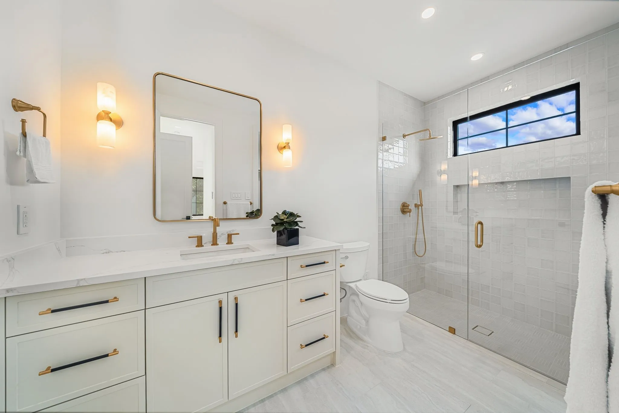 White vanity with a stone countertop, brass fixtures, a walk-in shower with a glass enclosure, and a built-in shower niche