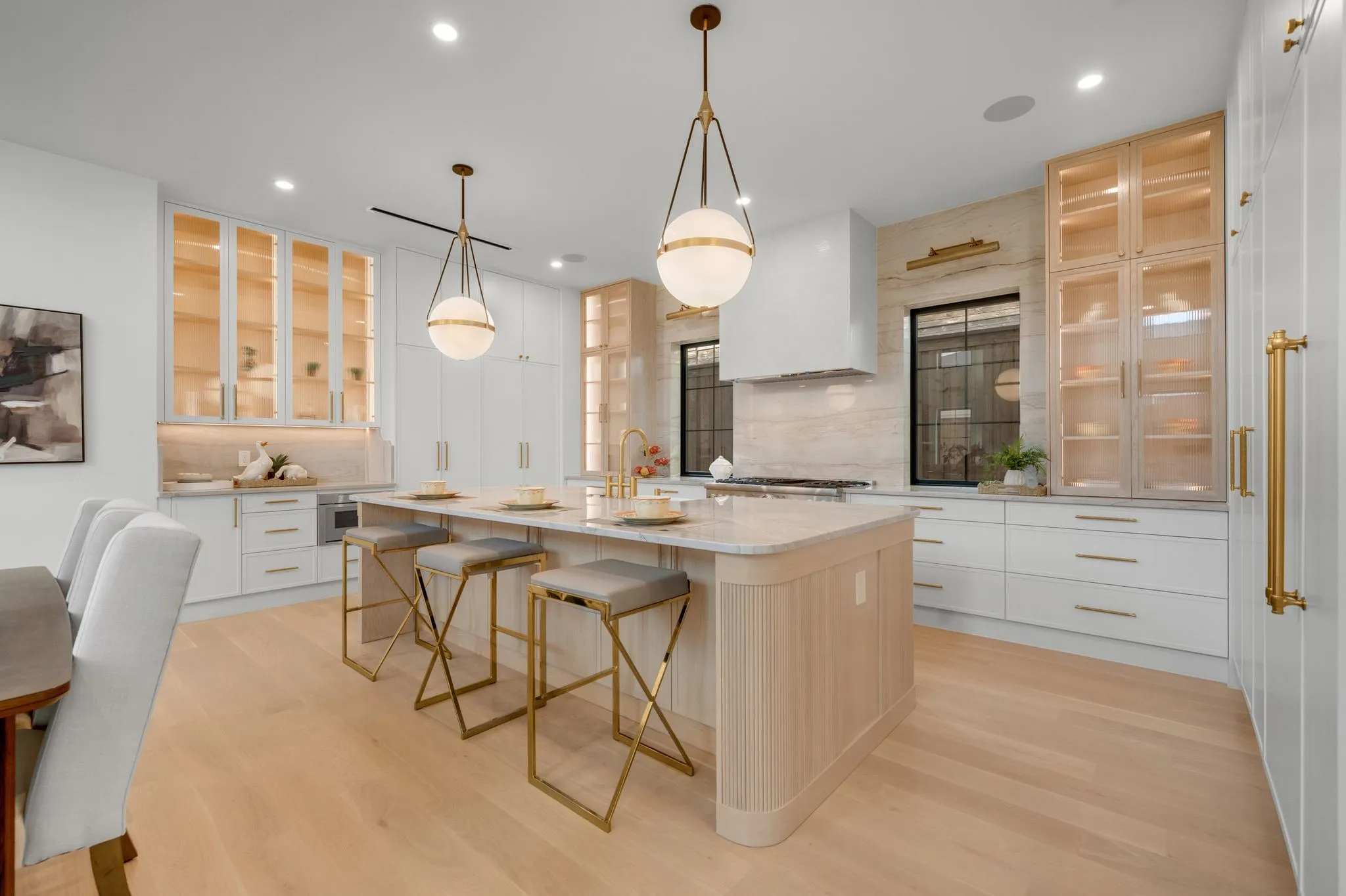 Spacious kitchen featuring an expansive central island, light wood-finish flooring, white cabinetry, integrated appliances, and recessed lighting