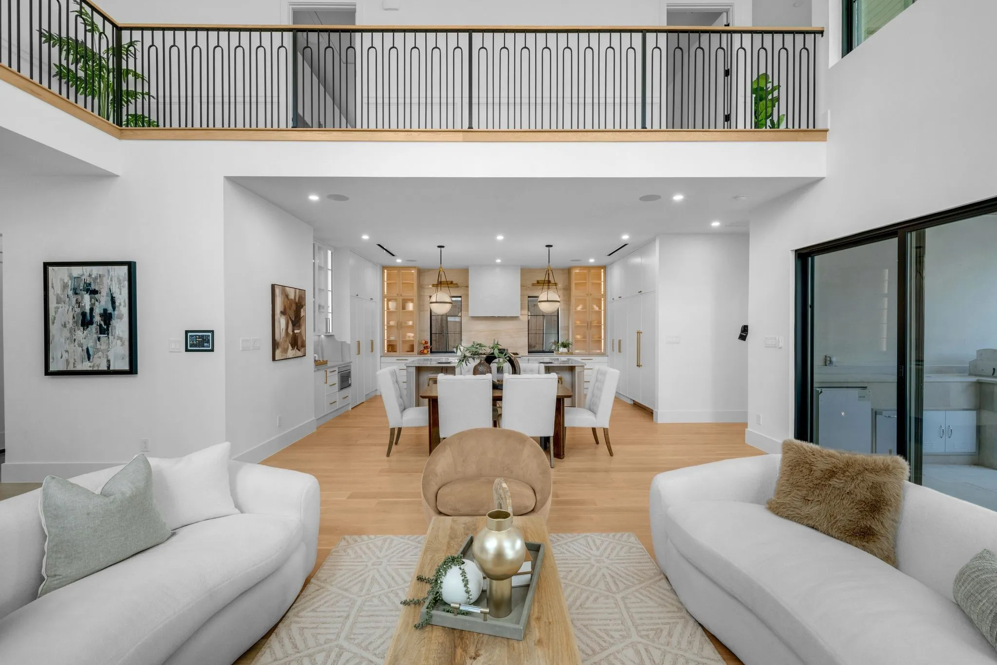 Two-story living space featuring an open-concept design, light wood-finish flooring, and a second-story balcony with metal railing