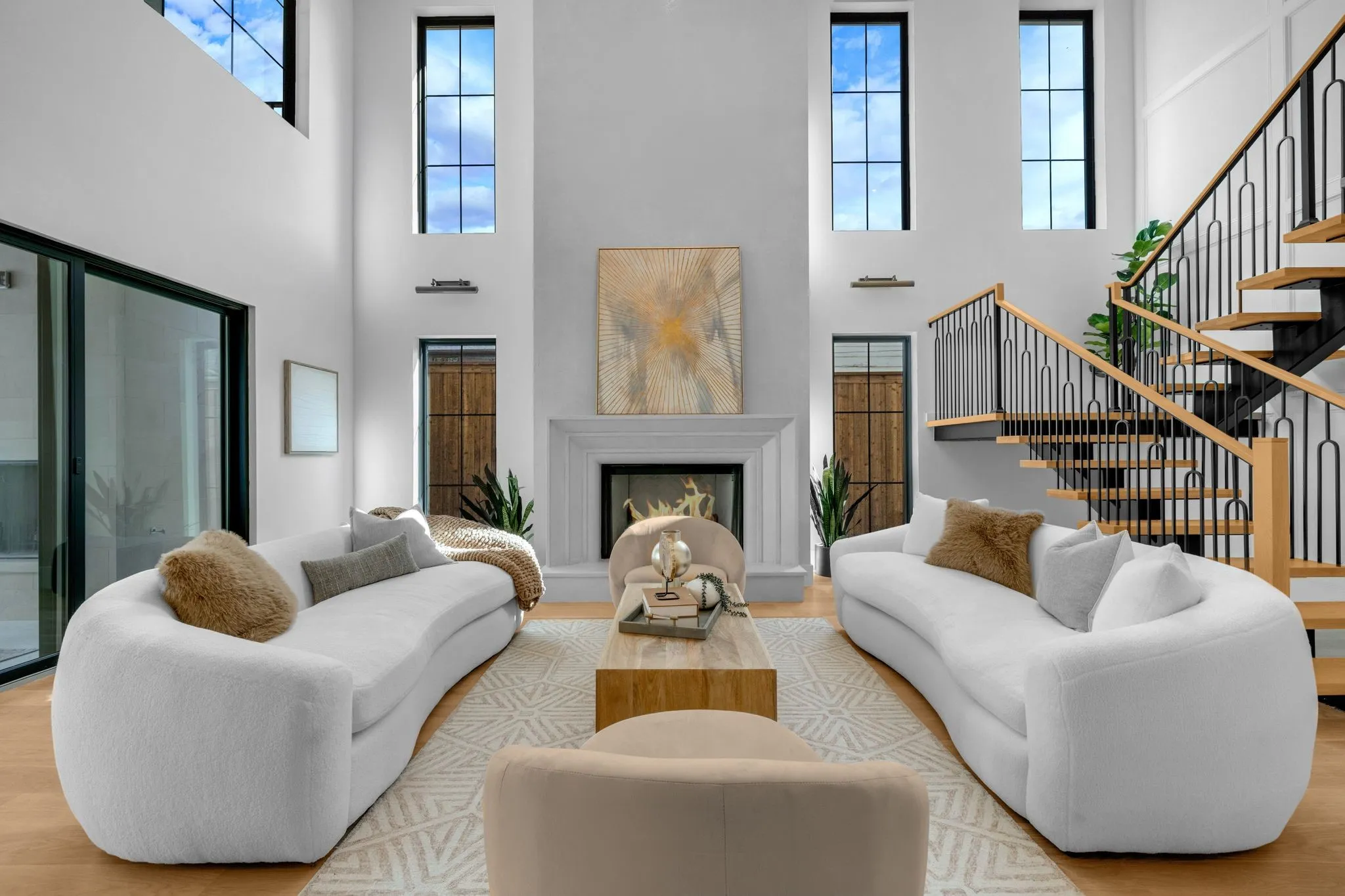 Two-story living area with high ceilings, a fireplace, and a light wood-finish staircase with black metal railing