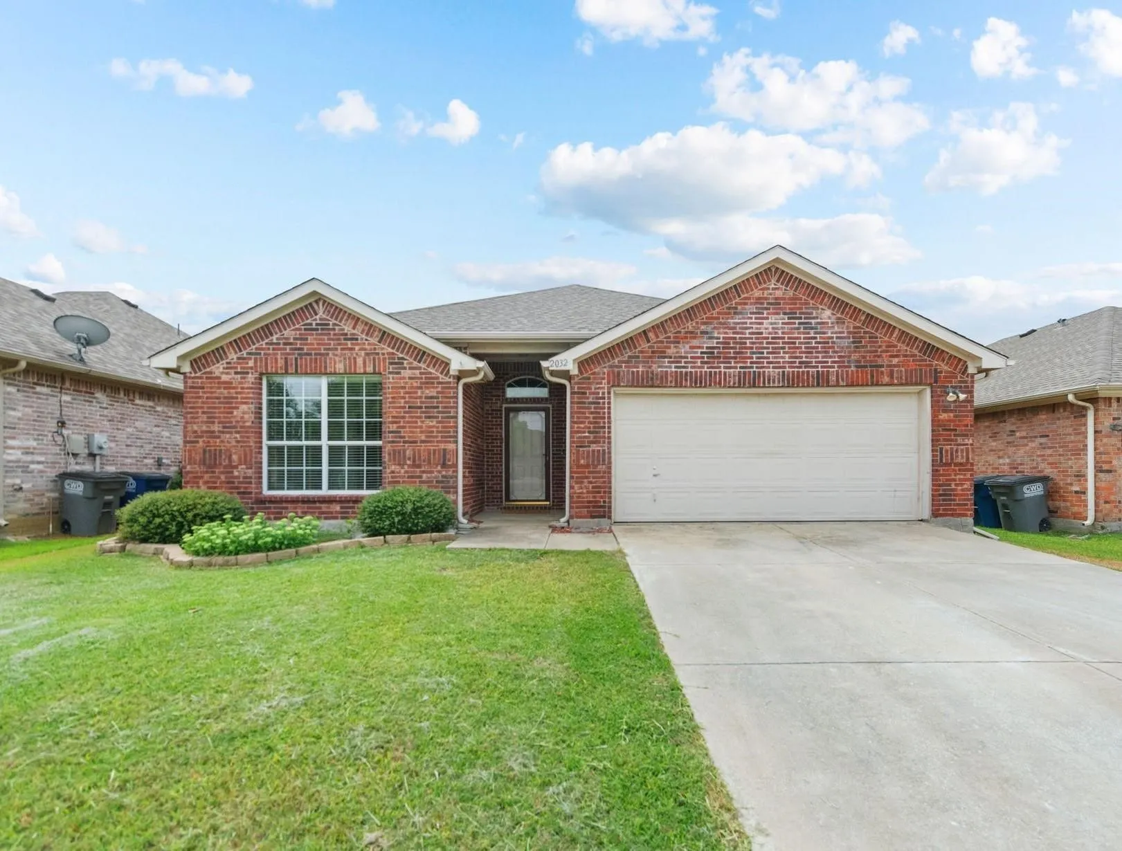 Brick exterior with a gabled roofline, an attached two-car garage, a concrete driveway, and a front yard with landscaping