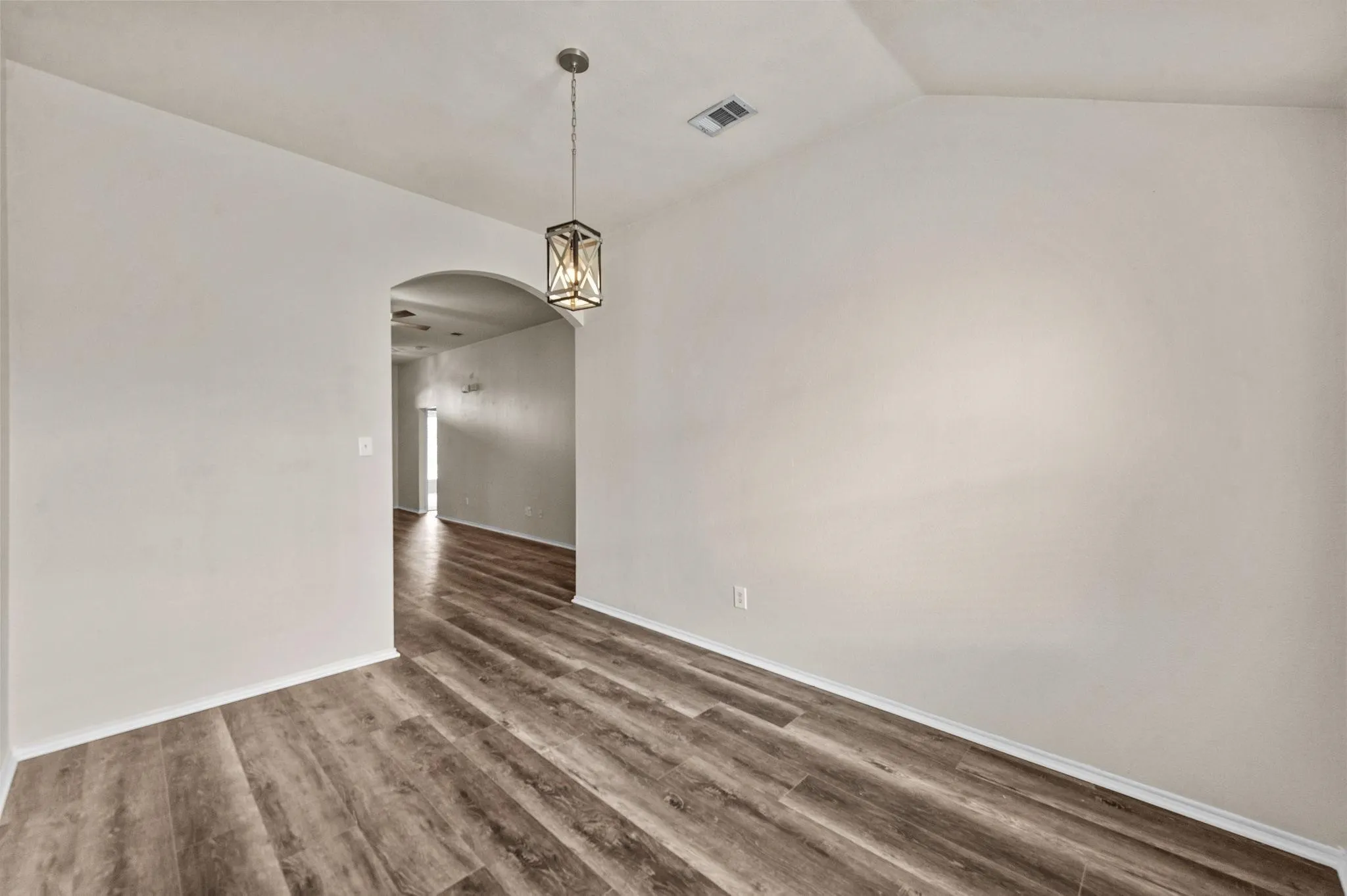 Vaulted ceiling, contemporary chandelier, wood-finish flooring, and arched doorway