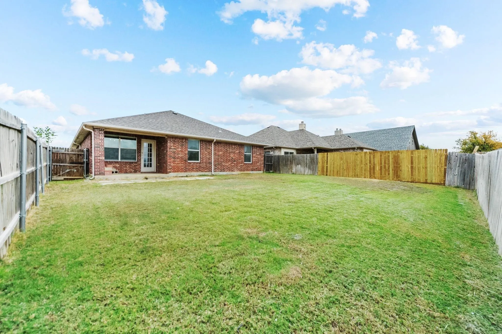 Expansive backyard featuring a manicured lawn, brick exterior, and a new wooden fence section
