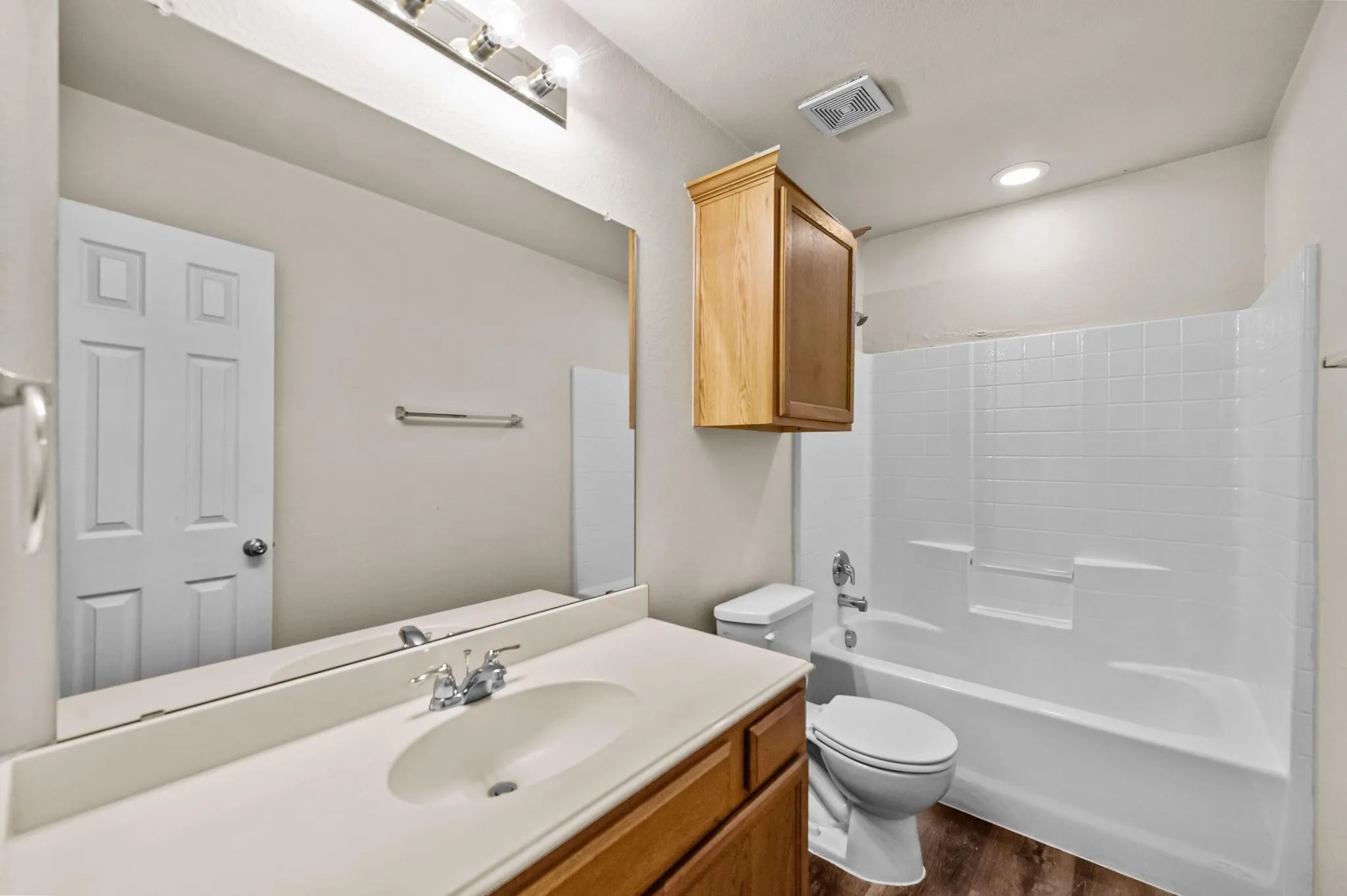 Bathroom featuring a vanity with an integrated sink, a full-width mirror, a wall-mounted light fixture, and wood-finish flooring