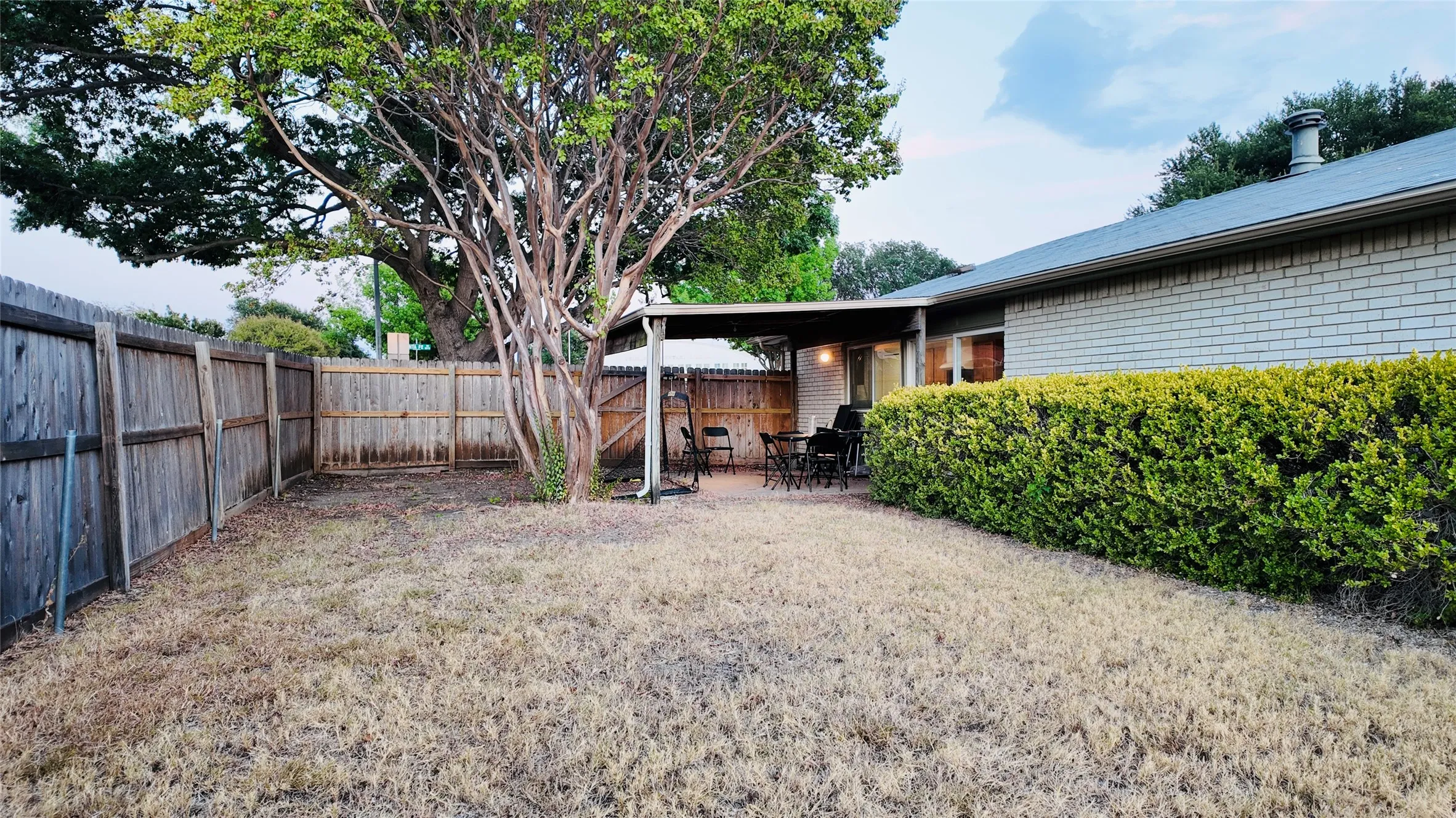 Expansive backyard featuring a mature tree, privacy fencing, a covered patio, and a manicured hedge