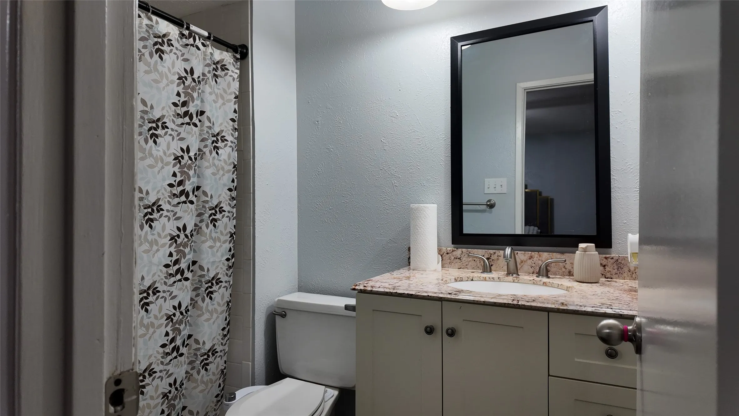 Bathroom featuring a single vanity with a stone countertop, an undermount sink, and a framed mirror
