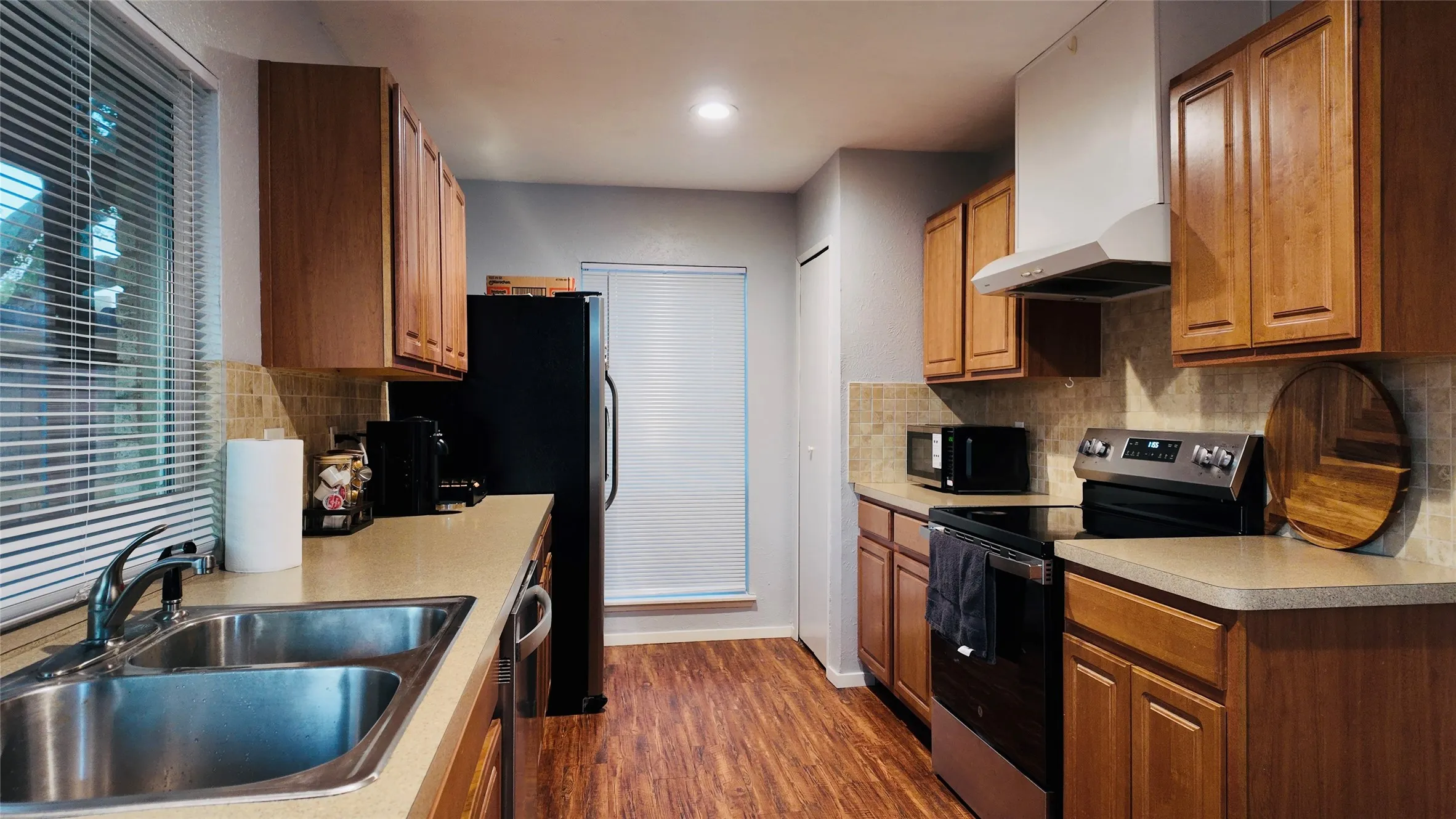 Kitchen featuring wood-finish flooring, wood cabinetry, stainless steel sink, tiled backsplash, and built-in​​‌​​​​‌​​‌‌​‌‌​​​‌‌​‌​‌​‌​​​‌​​ appliances