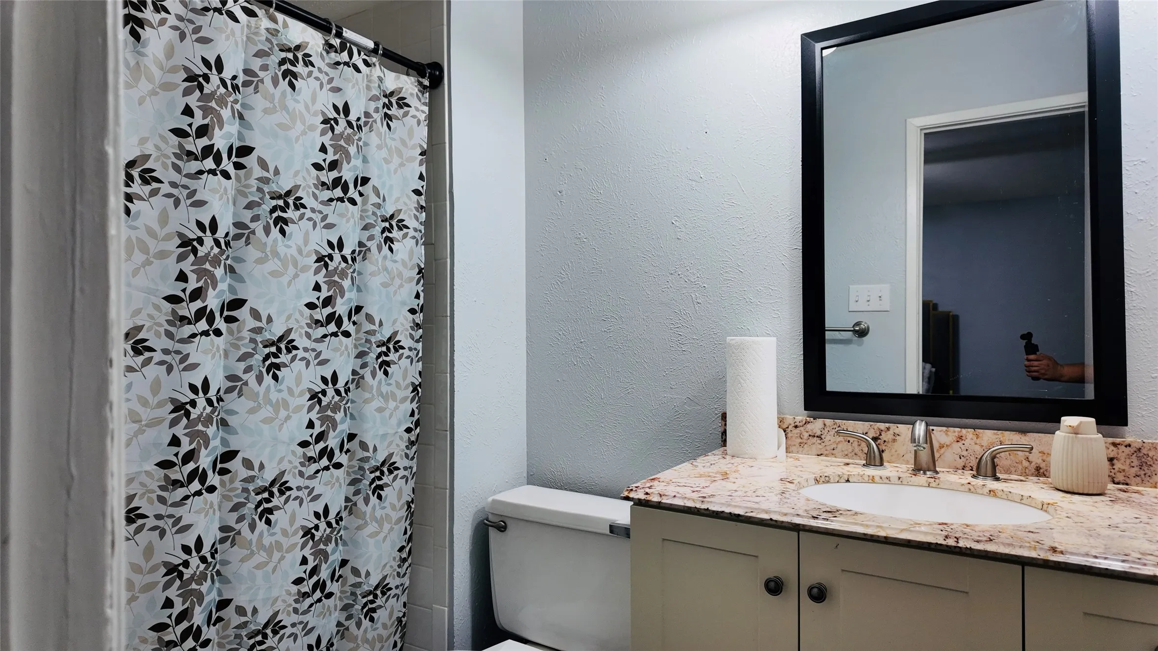 Vanity with a polished stone countertop and integrated sink, framed mirror, and a two-door cabinet with hardware