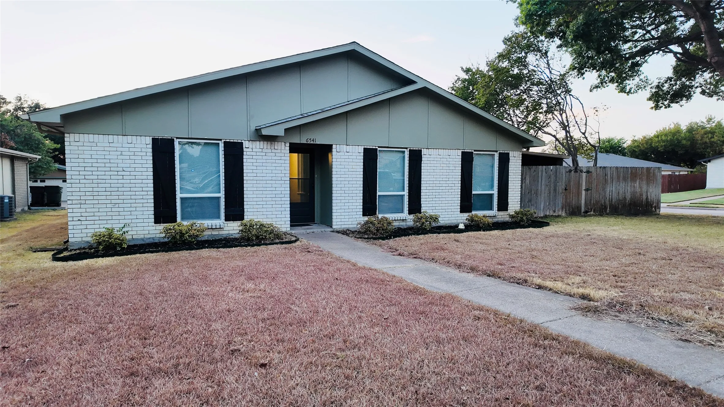 Single-story residence featuring light-colored brick exterior, dark shutters, and a sloped roofline