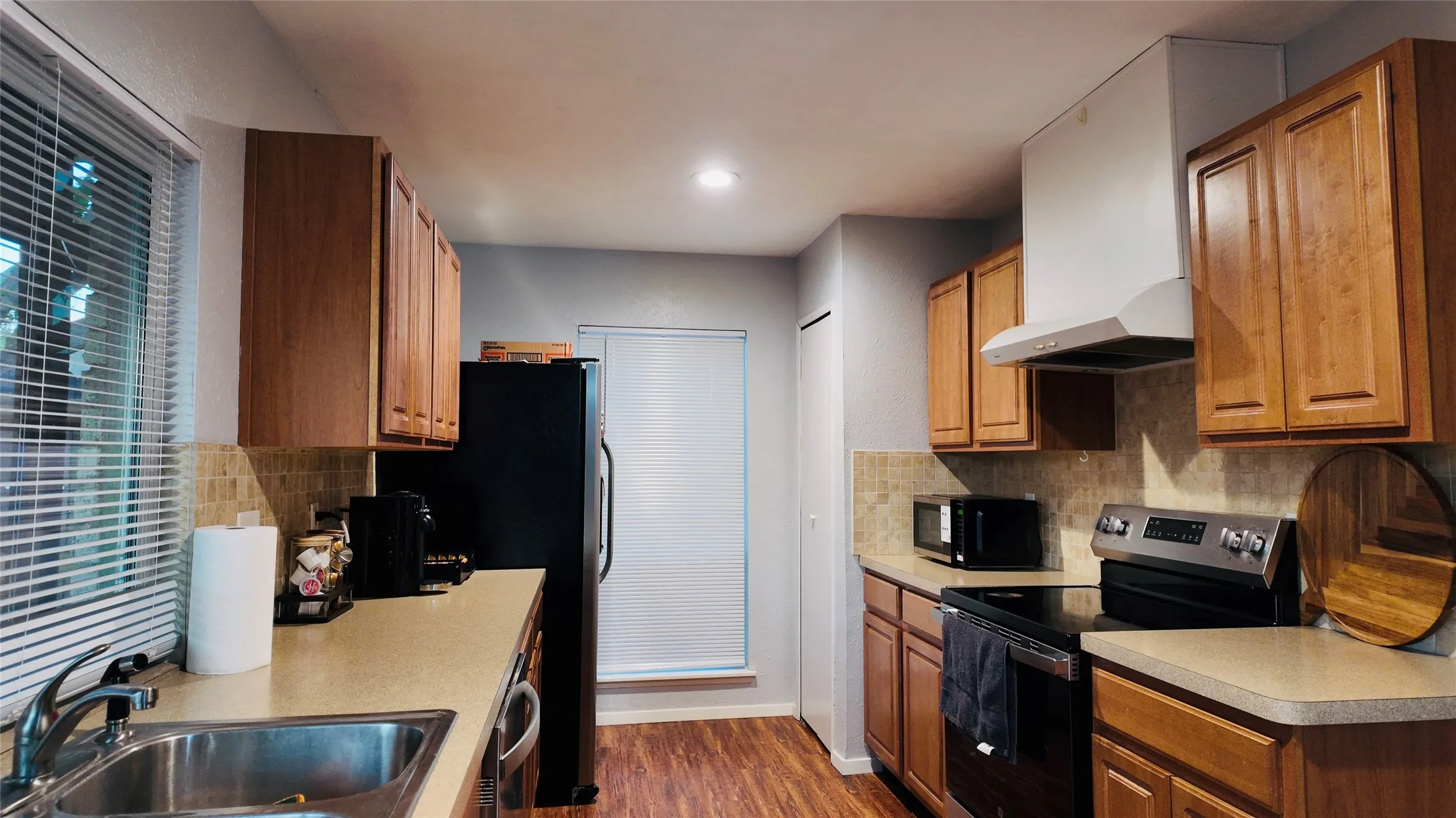Kitchen featuring wood-finish cabinetry, stainless steel sink, tile backsplash, and dark wood-look flooring
