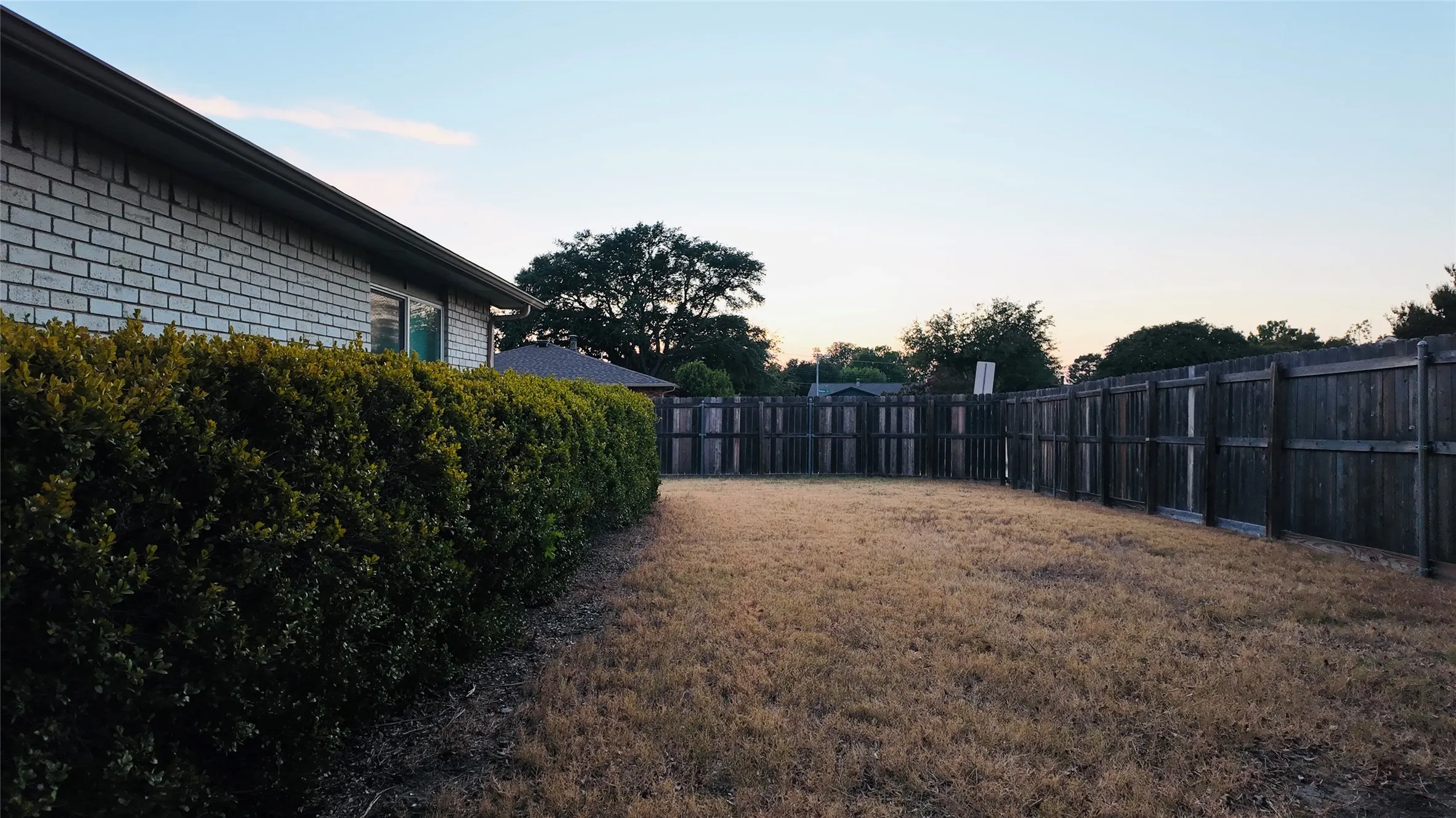 Fenced backyard featuring a brick exterior, well-maintained shrubbery, and a wood fence enclosure