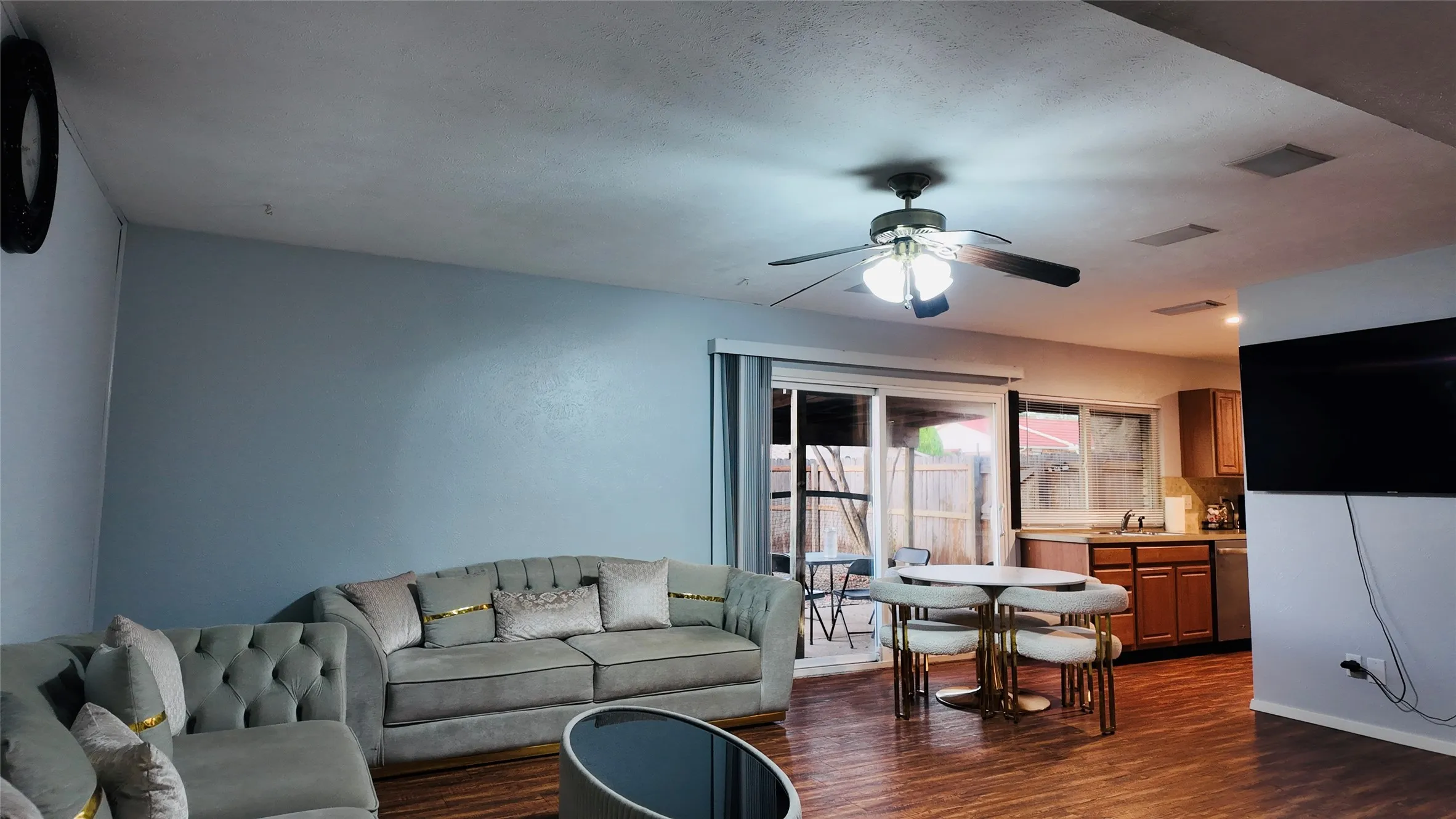 Wood-finish flooring throughout, ceiling fan with integrated lighting, sliding glass door access to exterior, kitchen with wood cabinetry and stainless steel appliances, recessed ceiling lights