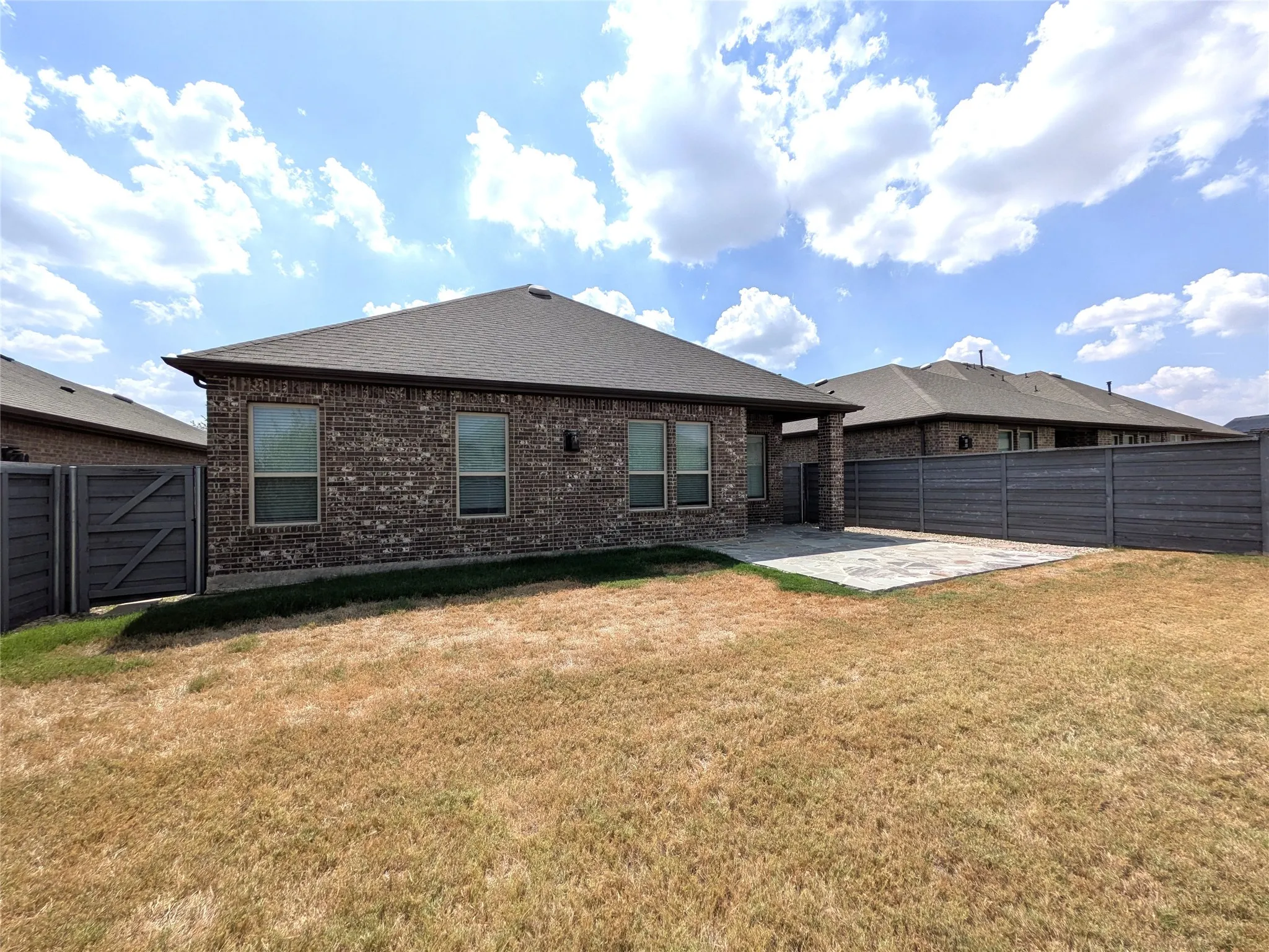 Brick exterior with multiple windows, a shingled roof, a paved patio, and a privacy fence