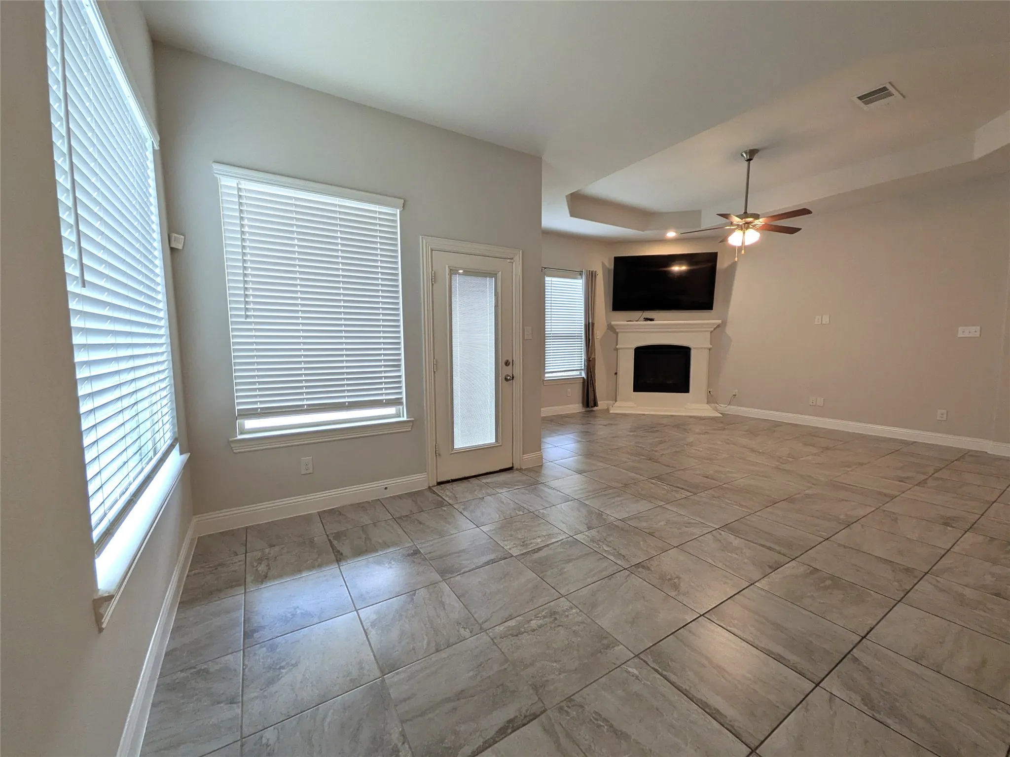Spacious living area featuring tile flooring, a fireplace with a mantel, a ceiling fan, and a tray ceiling