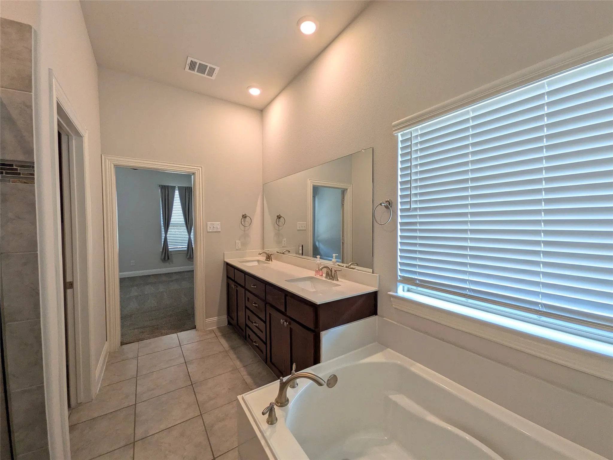 Tiled flooring leading to a built-in soaking tub, a dual vanity with undermount sinks, and a large mirror