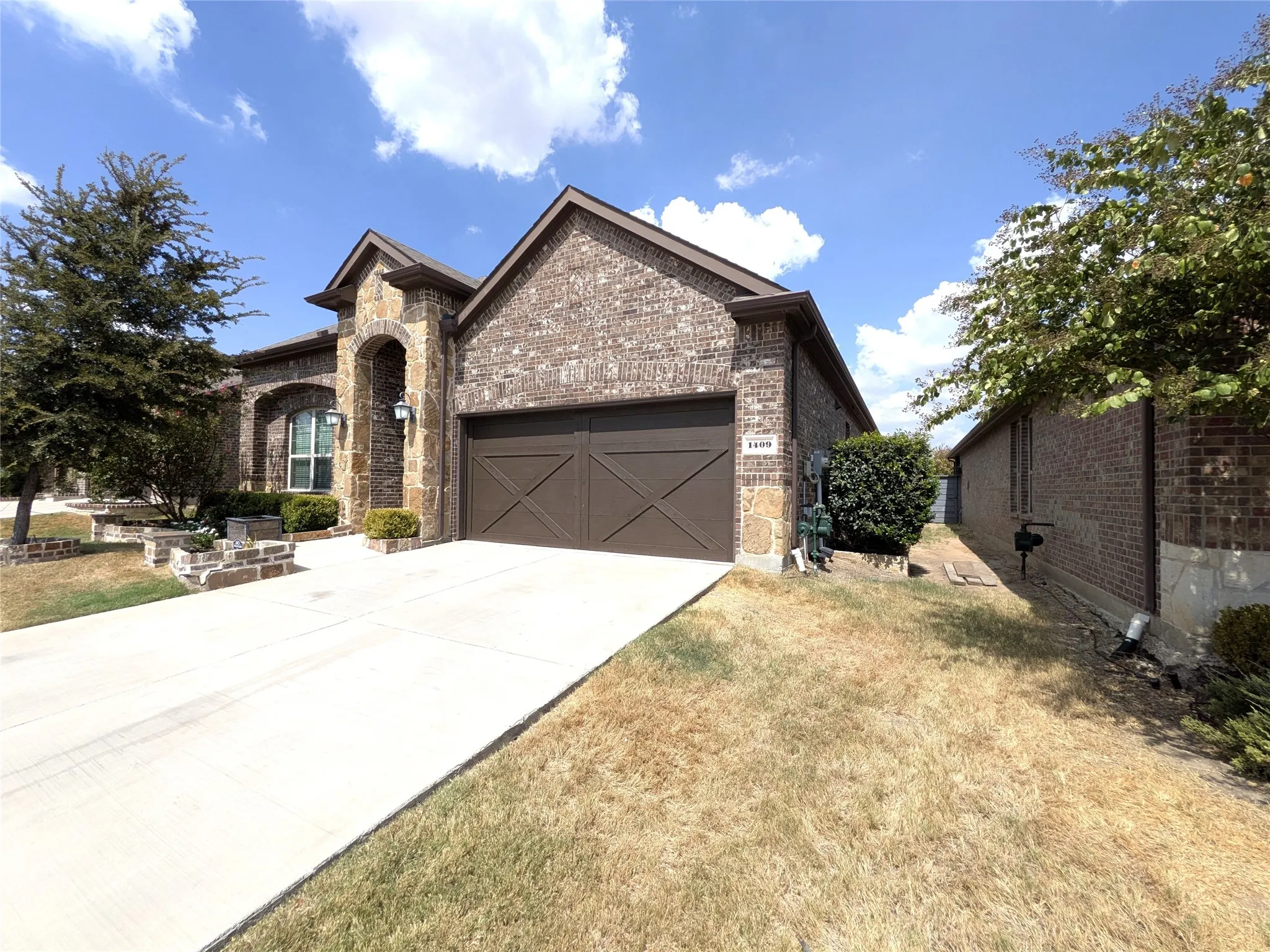 Brick and stone exterior featuring an arched entryway, attached garage with decorative doors, and a concrete driveway