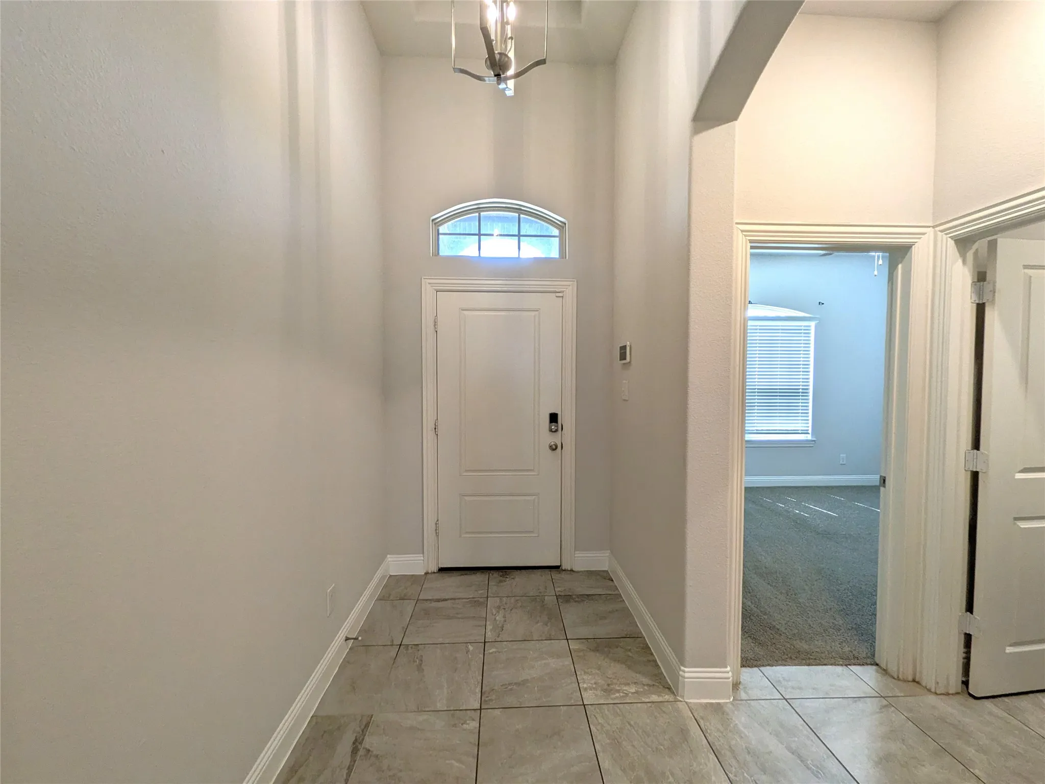 Foyer featuring high ceilings, tile flooring, an arched transom window, and a contemporary ceiling light fixture