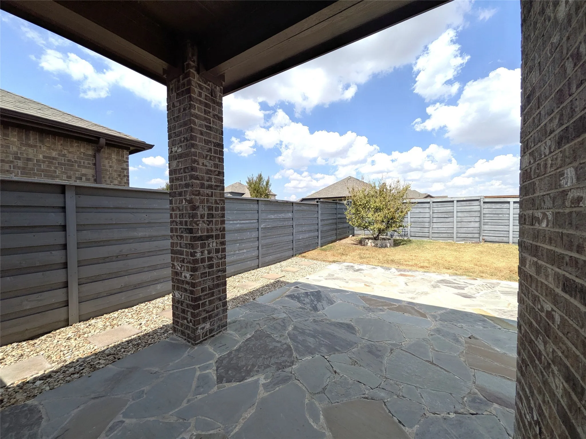 Covered patio featuring a flagstone surface, brick columns, and a gravel border