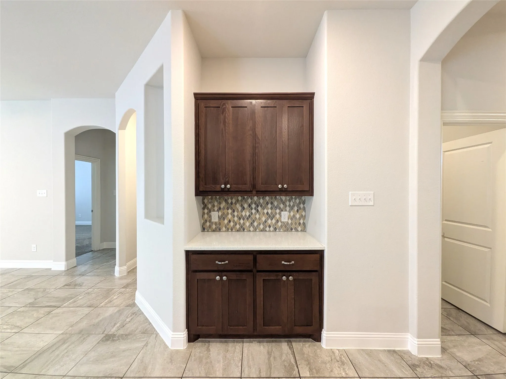 Built-in cabinetry with a light-toned countertop, mosaic tile backsplash, and tile flooring