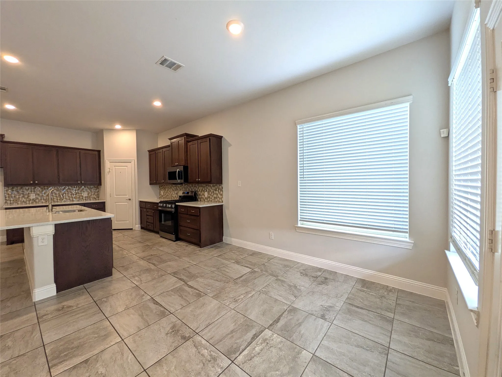 Kitchen featuring dark wood cabinetry, a center island with sink, stainless steel appliances, mosaic tile backsplash, and tile flooring