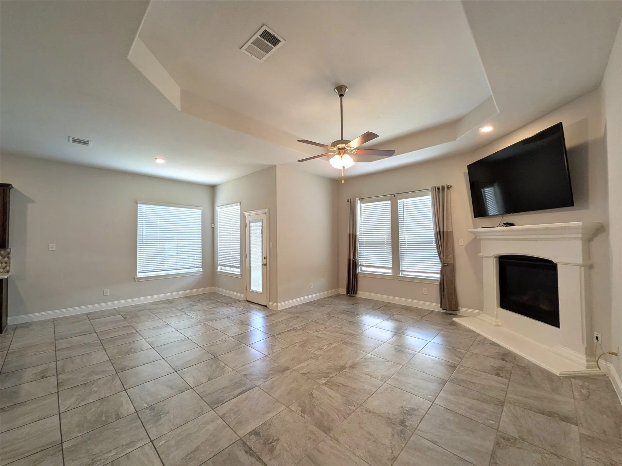 Tray ceiling with a ceiling fan, recessed lighting, tile flooring, and a corner fireplace with a white mantel