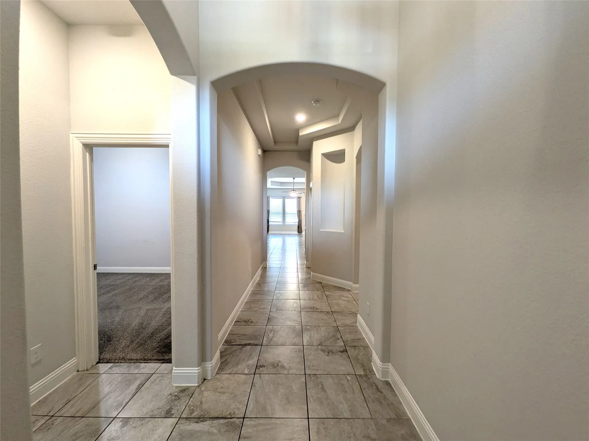 Hallway featuring tile flooring, arched doorways, recessed lighting, and tray ceilings