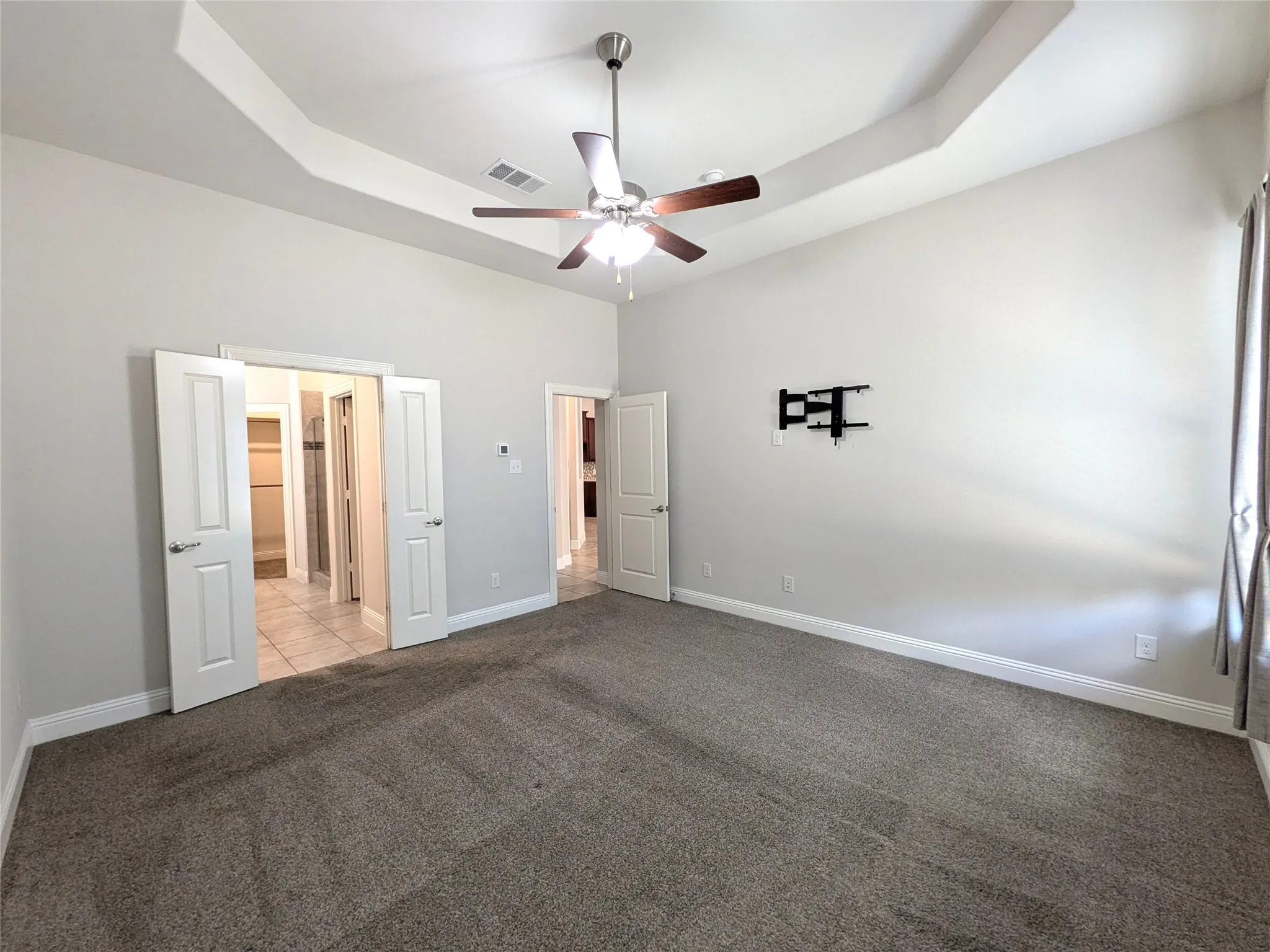 Recessed tray ceiling with a ceiling fan, light gray wall paint, and gray carpeting