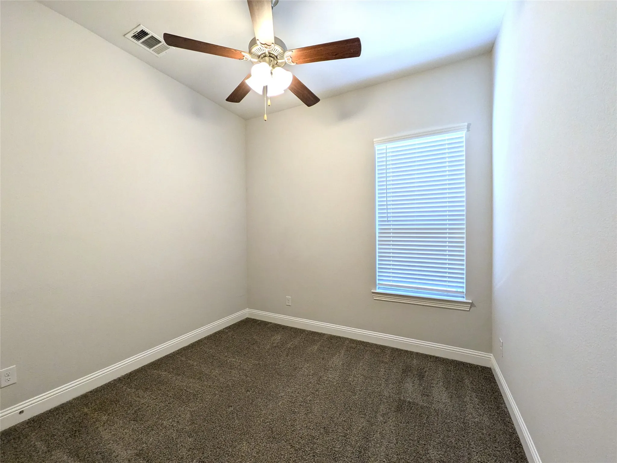 Carpeted room featuring a ceiling fan with light fixture and a window with blinds