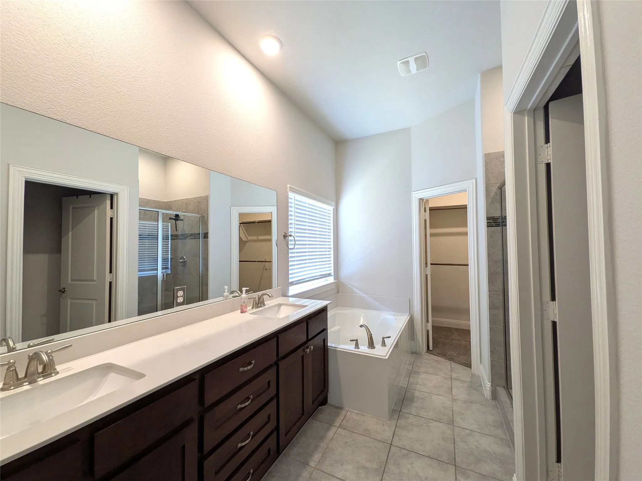 Dual vanities with integrated sinks, dark wood-finish cabinetry, a large soaking tub, and a separate glass-enclosed shower